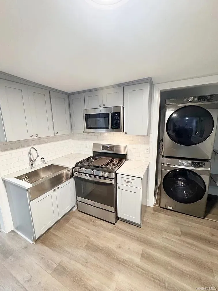 Kitchen with appliances with stainless steel finishes, estacked washer and dryer, light stone counters, and light wood finished floors Kitchen with appliances with stainless steel finishes, estacked washer and dryer, light stone counters, and light wood finished floors