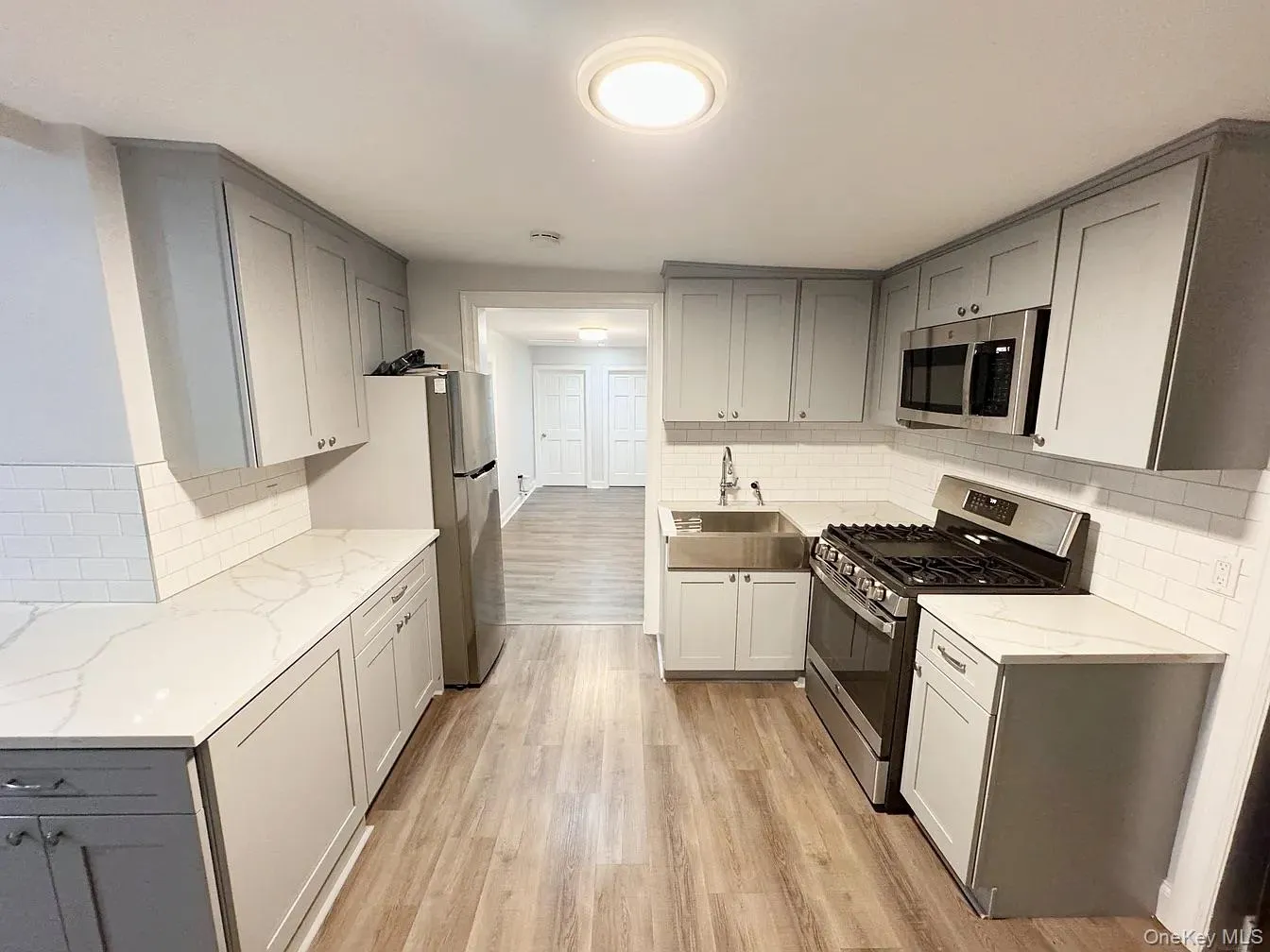 Kitchen with gray cabinets, appliances with stainless steel finishes, light stone countertops, and light wood-style flooring Kitchen with gray cabinets, appliances with stainless steel finishes, light stone countertops, and light wood-style flooring