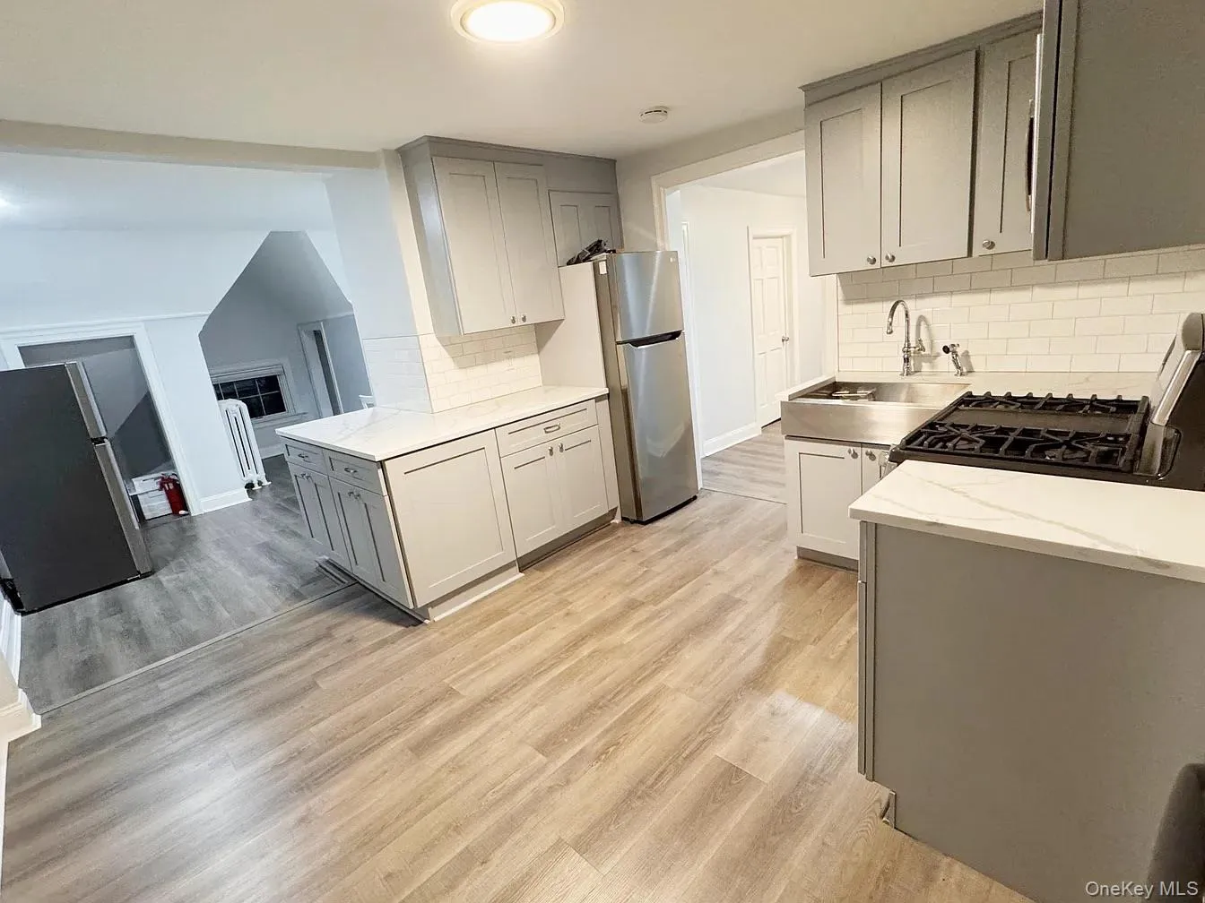 Kitchen featuring gray cabinets, freestanding refrigerator, light stone counters, light wood finished floors, and range with gas cooktop Kitchen featuring gray cabinets, freestanding refrigerator, light stone counters, light wood finished floors, and range with gas cooktop