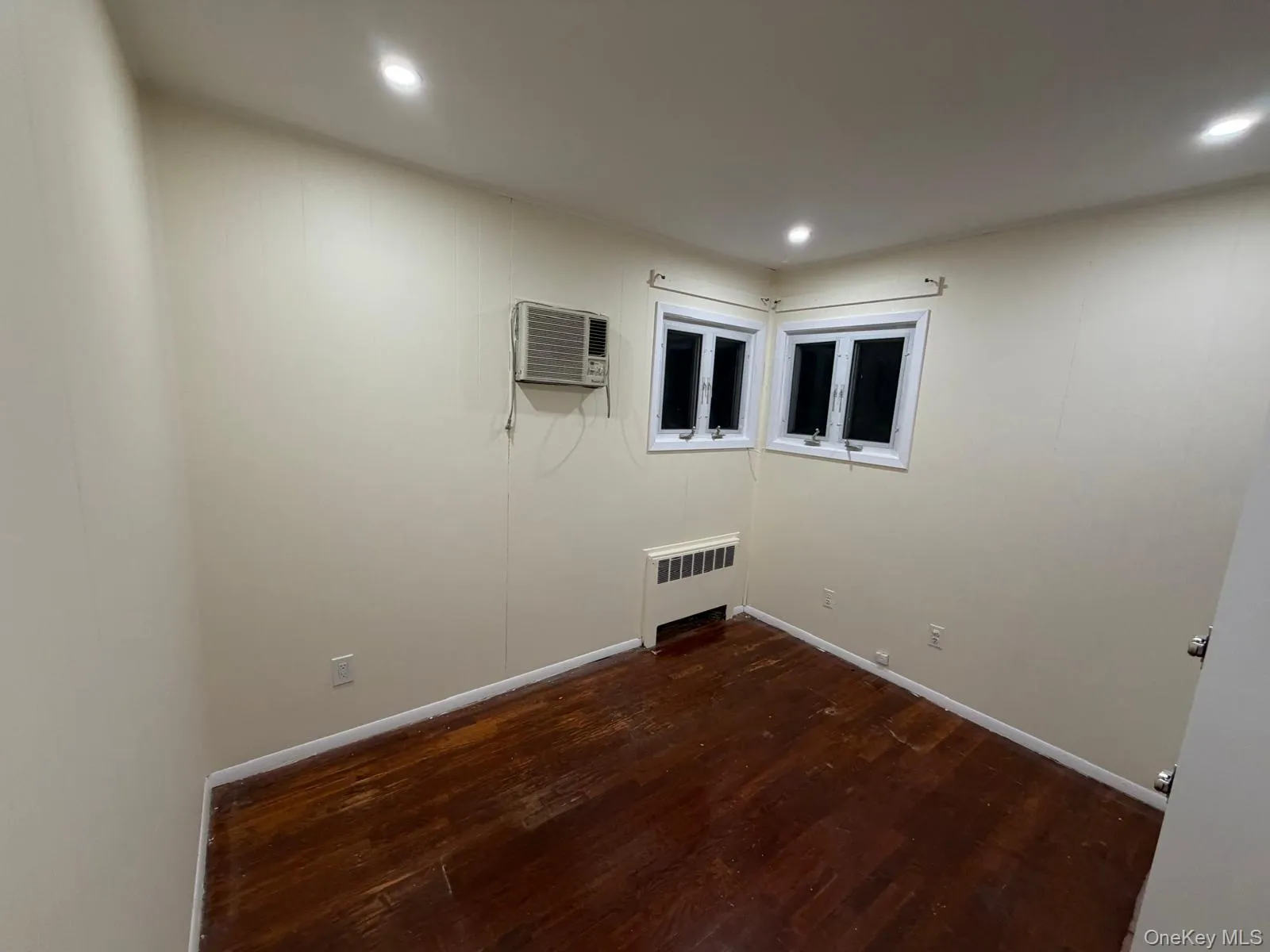 Empty room with dark wood-style floors, radiator, a wall mounted AC, and recessed lighting Empty room with dark wood-style floors, radiator, a wall mounted AC, and recessed lighting