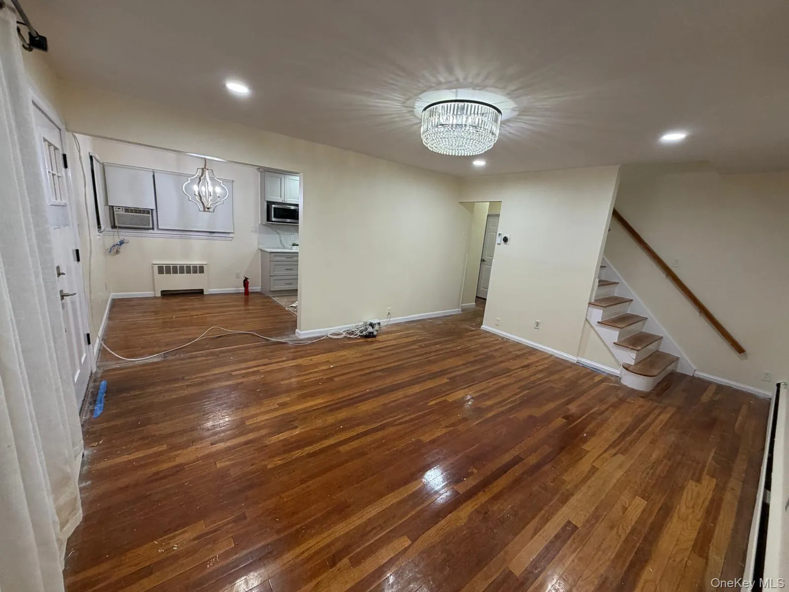 Unfurnished living room with a chandelier, recessed lighting, dark wood-style floors, stairway, and a baseboard heating unit Unfurnished living room with a chandelier, recessed lighting, dark wood-style floors, stairway, and a baseboard heating unit