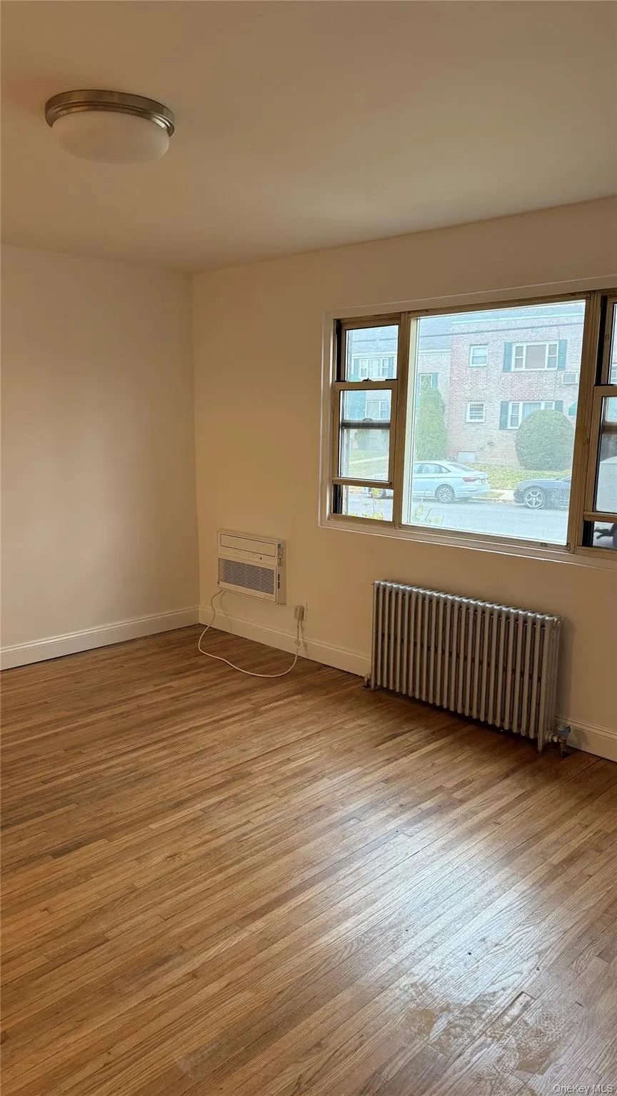 Unfurnished room featuring radiator heating unit, light wood finished floors, and a wall mounted AC Unfurnished room featuring radiator heating unit, light wood finished floors, and a wall mounted AC