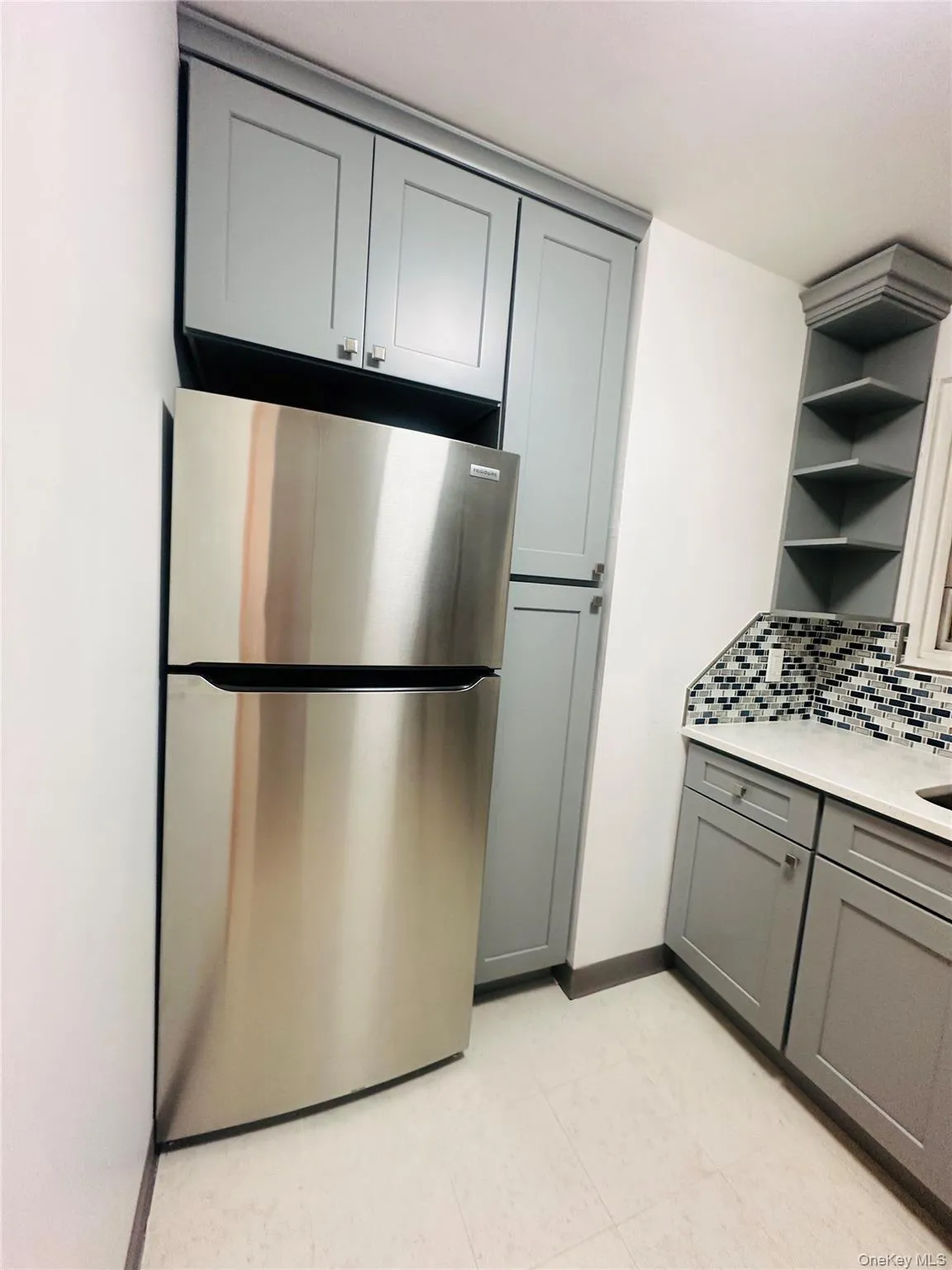 Kitchen with gray cabinets, freestanding refrigerator, open shelves, light stone counters, and backsplash Kitchen with gray cabinets, freestanding refrigerator, open shelves, light stone counters, and backsplash