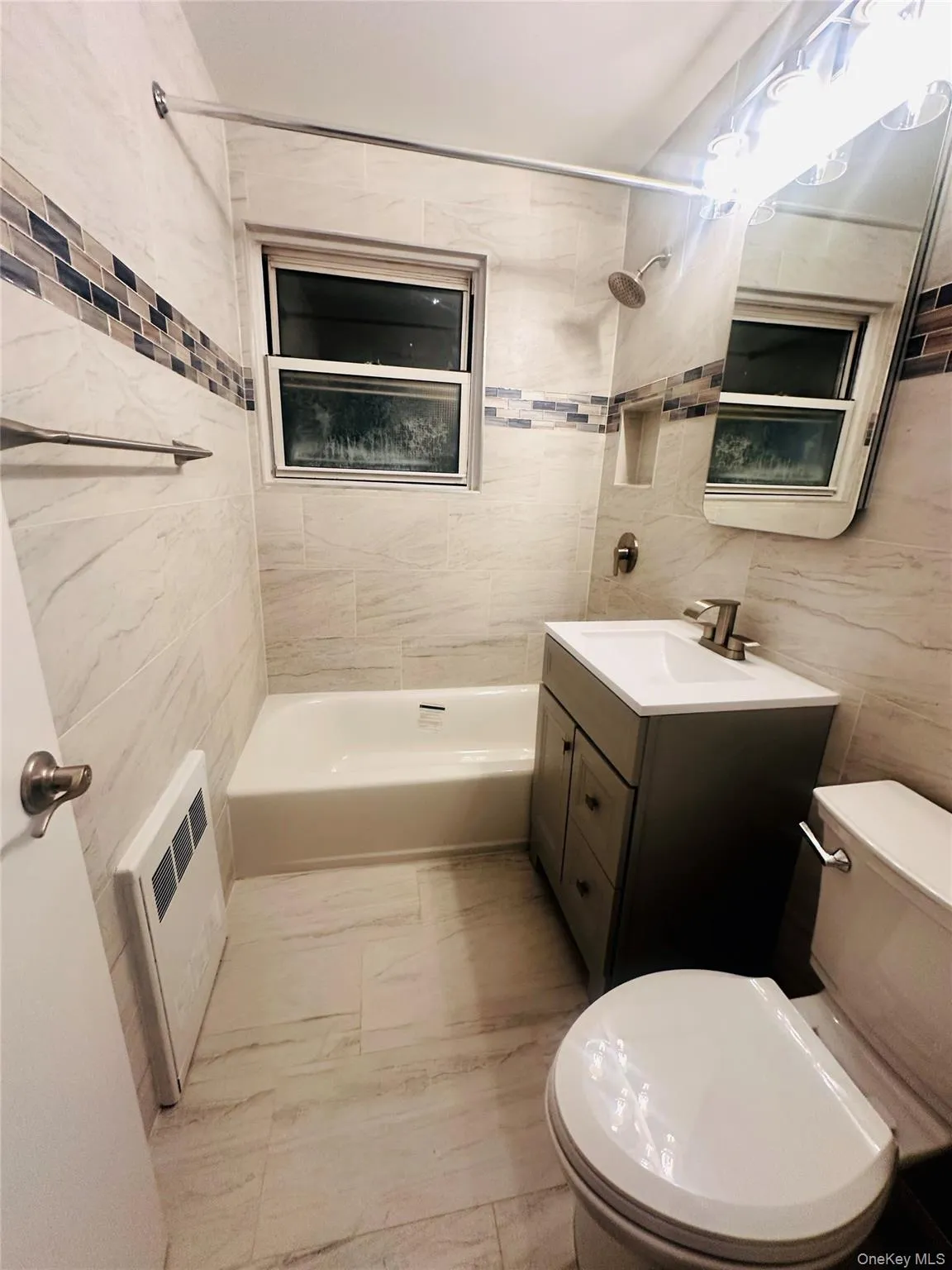 Bathroom featuring vanity, shower combination, tile walls, light marble finish flooring, and heating unit Bathroom featuring vanity, shower combination, tile walls, light marble finish flooring, and heating unit