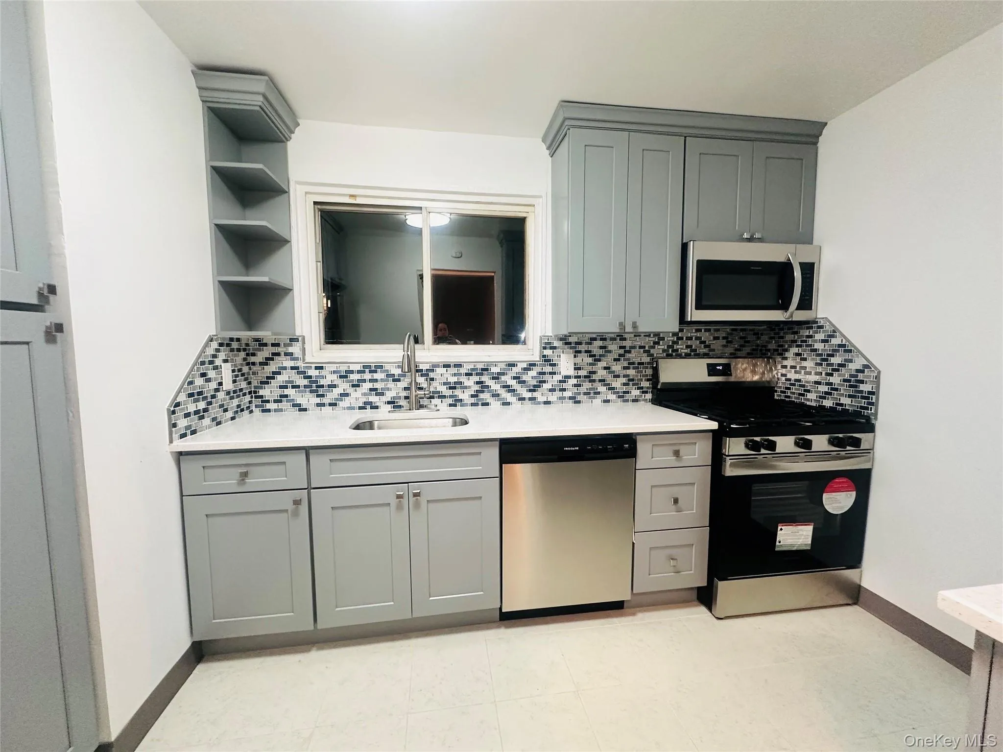 Kitchen with gray cabinets, appliances with stainless steel finishes, open shelves, light stone counters, and decorative backsplash Kitchen with gray cabinets, appliances with stainless steel finishes, open shelves, light stone counters, and decorative backsplash