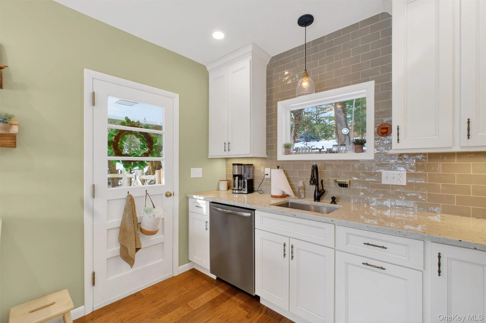 Kitchen with decorative backsplash, white cabinets, dishwasher, light stone countertops, and light wood-style flooring Kitchen with decorative backsplash, white cabinets, dishwasher, light stone countertops, and light wood-style flooring