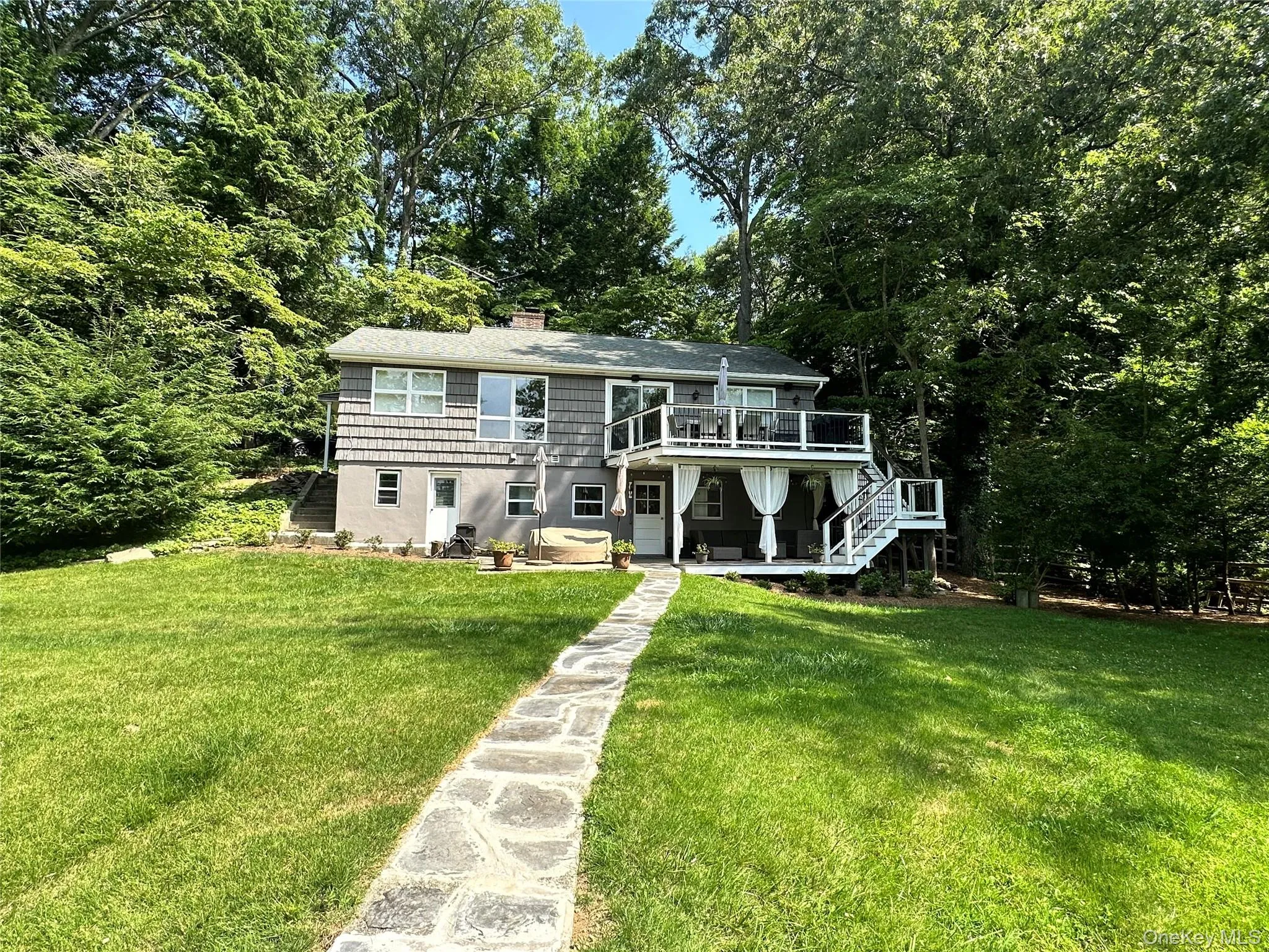 View of front facade featuring stairs, a chimney, a front lawn, a wooden deck, and a patio View of front facade featuring stairs, a chimney, a front lawn, a wooden deck, and a patio