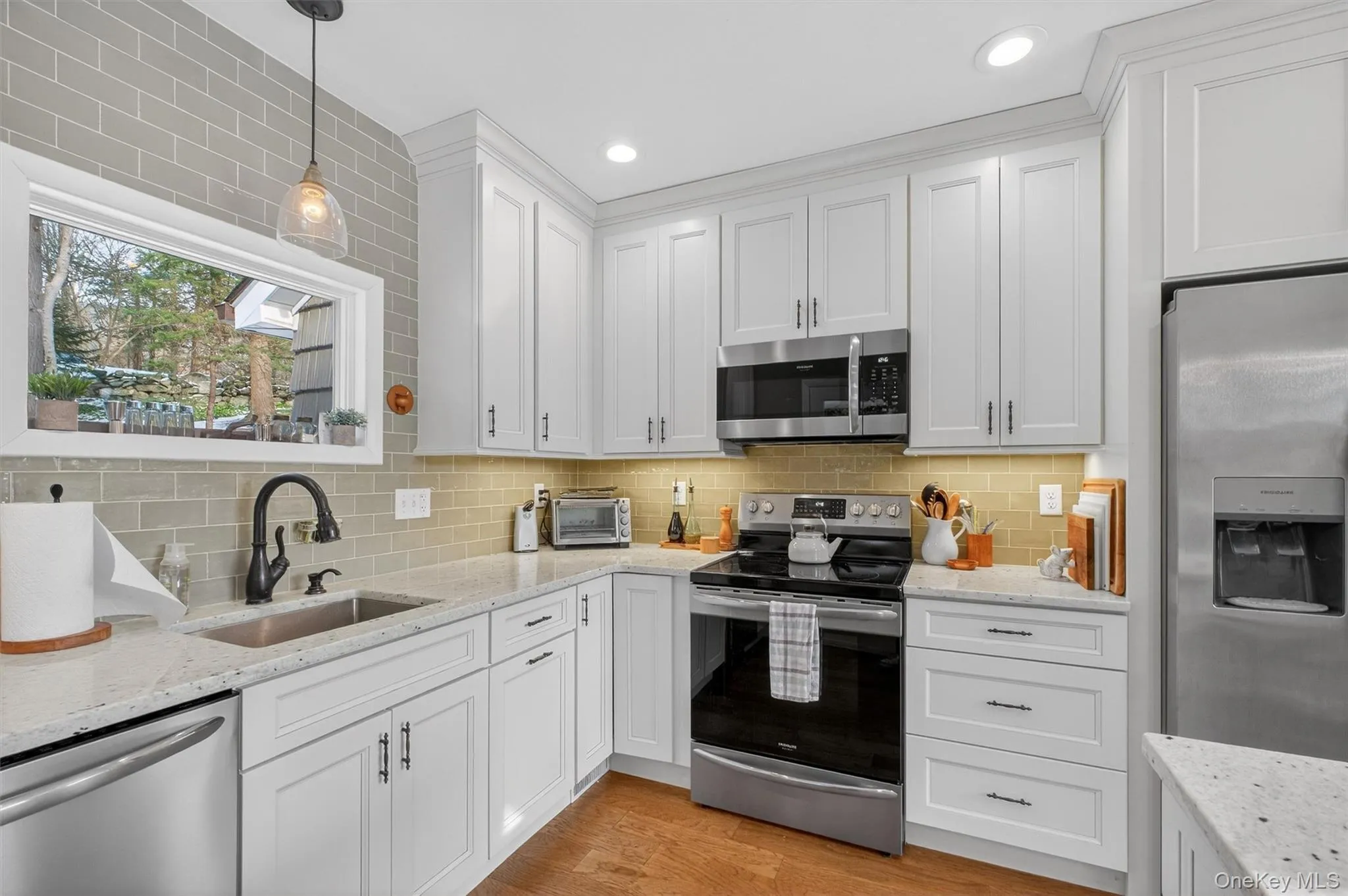 Kitchen with appliances with stainless steel finishes, hanging light fixtures, light stone counters, and white cabinets Kitchen with appliances with stainless steel finishes, hanging light fixtures, light stone counters, and white cabinets