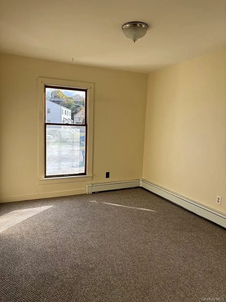 Empty room featuring dark colored carpet and a baseboard radiator Empty room featuring dark colored carpet and a baseboard radiator