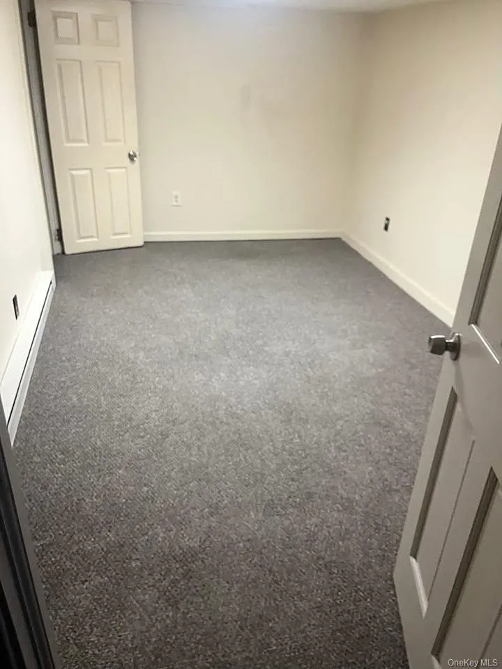 Unfurnished room with dark colored carpet and a baseboard heating unit Unfurnished room with dark colored carpet and a baseboard heating unit