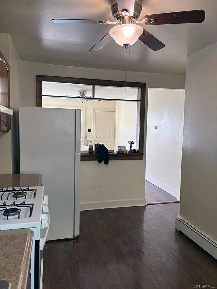 Kitchen featuring white gas range, a baseboard radiator, dark wood-style flooring, freestanding refrigerator, and under cabinet range hood Kitchen featuring white gas range, a baseboard radiator, dark wood-style flooring, freestanding refrigerator, and under cabinet range hood
