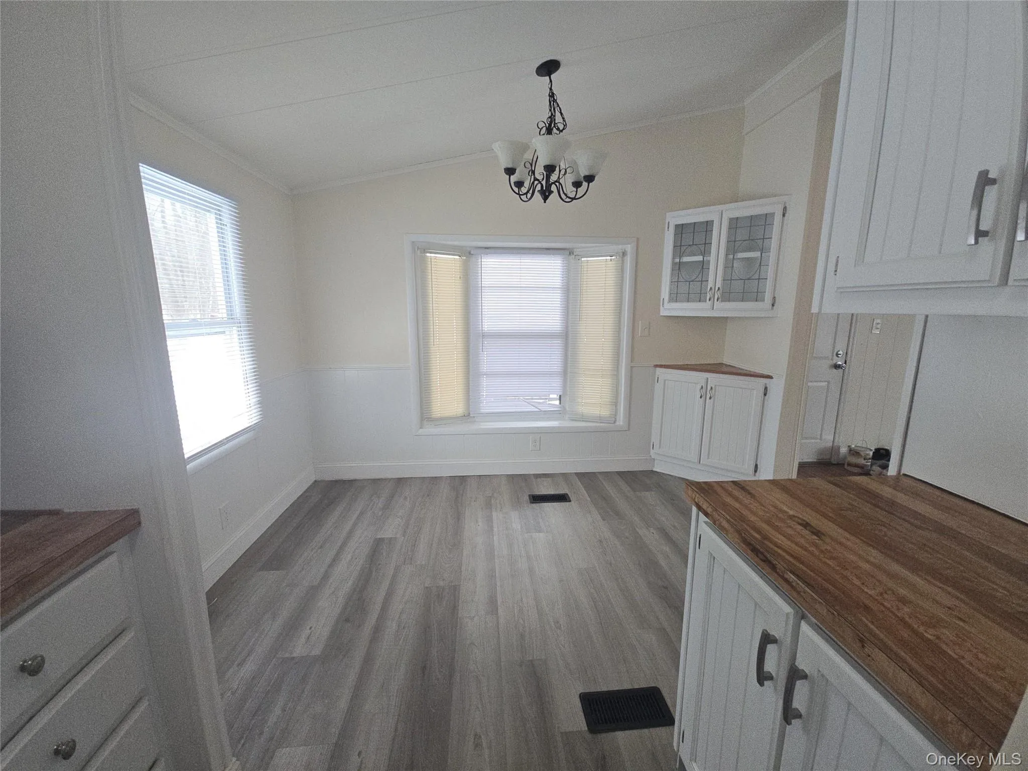 Unfurnished dining area with lofted ceiling, light wood finished floors, a chandelier, and crown molding Unfurnished dining area with lofted ceiling, light wood finished floors, a chandelier, and crown molding