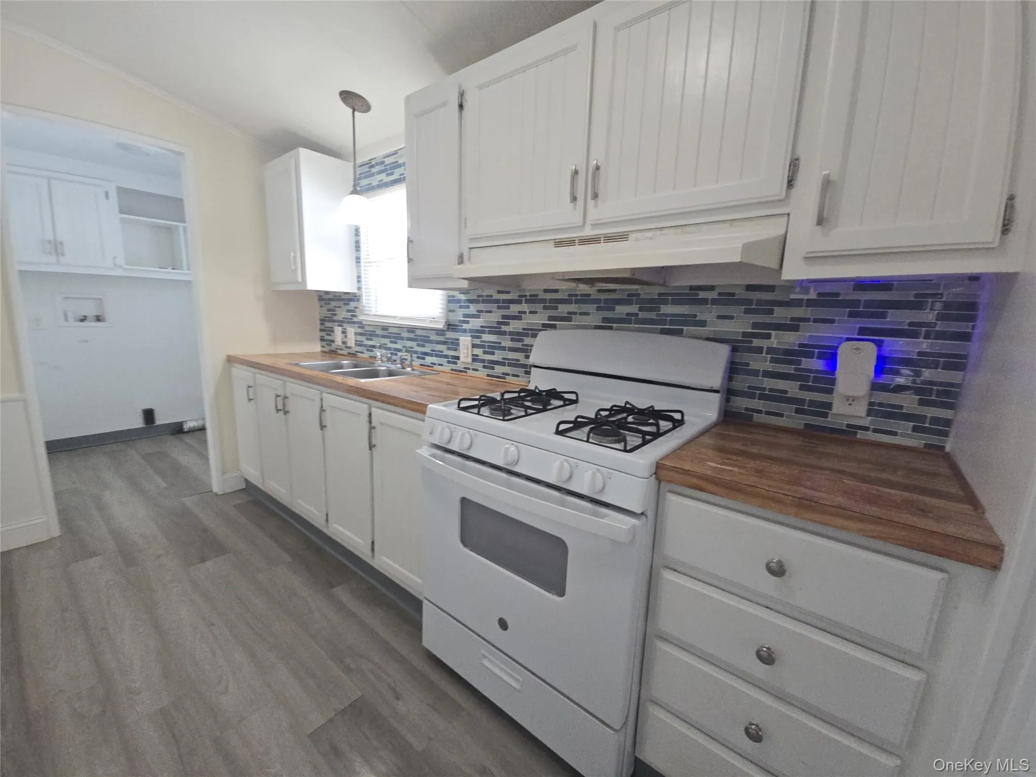 Kitchen featuring white range with gas stovetop, pendant lighting, under cabinet range hood, dark wood-style flooring, and white cabinets Kitchen featuring white range with gas stovetop, pendant lighting, under cabinet range hood, dark wood-style flooring, and white cabinets