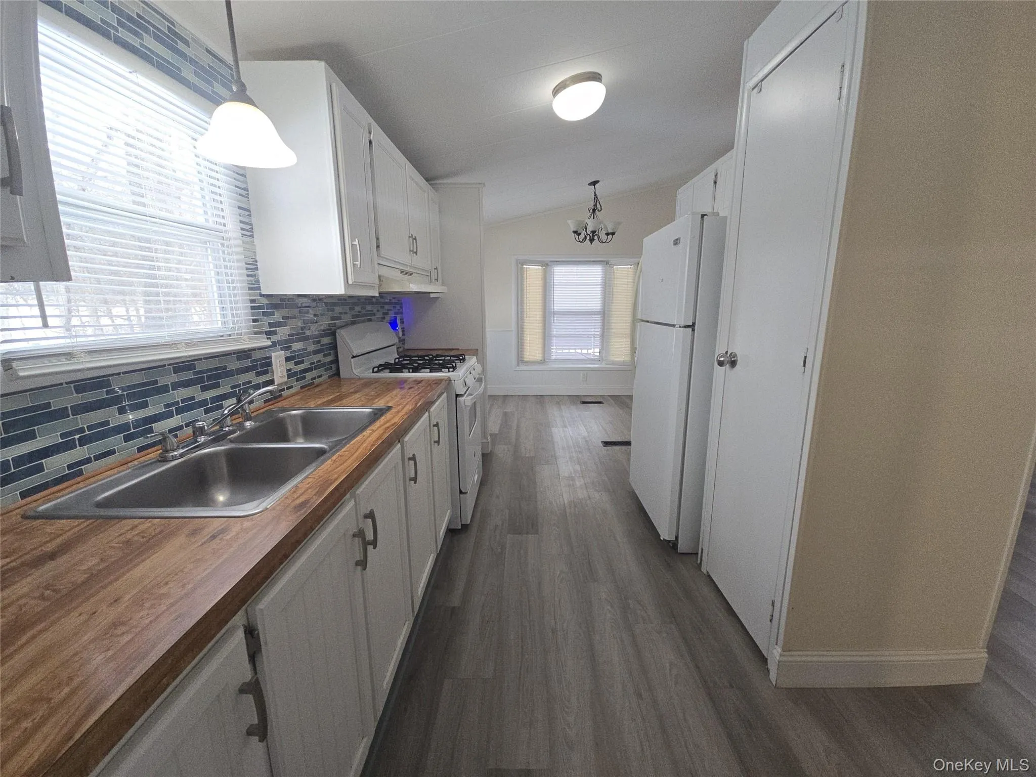 Kitchen with butcher block counters, hanging light fixtures, white cabinetry, white appliances, and vaulted ceiling Kitchen with butcher block counters, hanging light fixtures, white cabinetry, white appliances, and vaulted ceiling