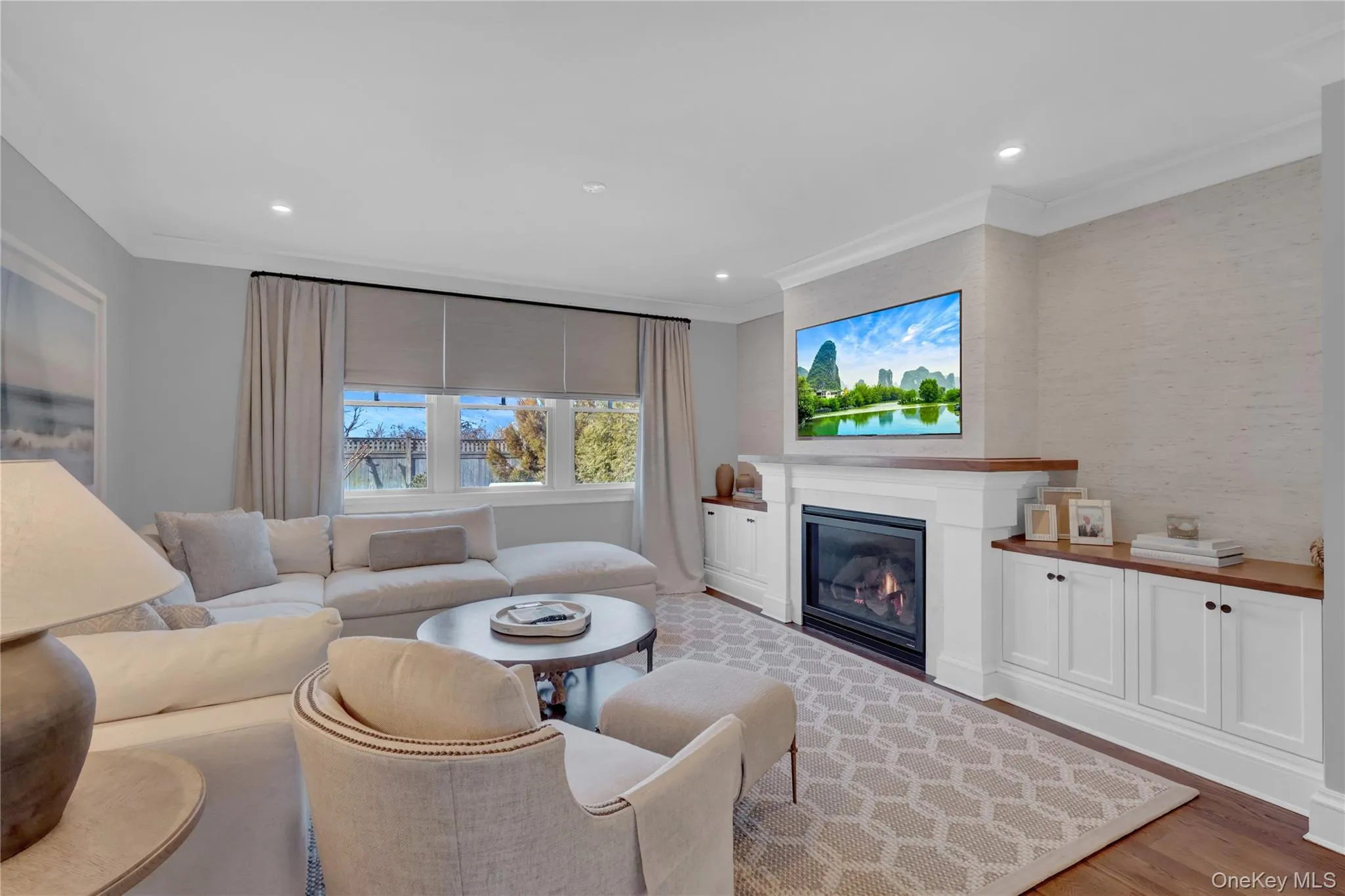 Living area featuring a glass covered fireplace, light wood finished floors, crown molding, and recessed lighting Living area featuring a glass covered fireplace, light wood finished floors, crown molding, and recessed lighting