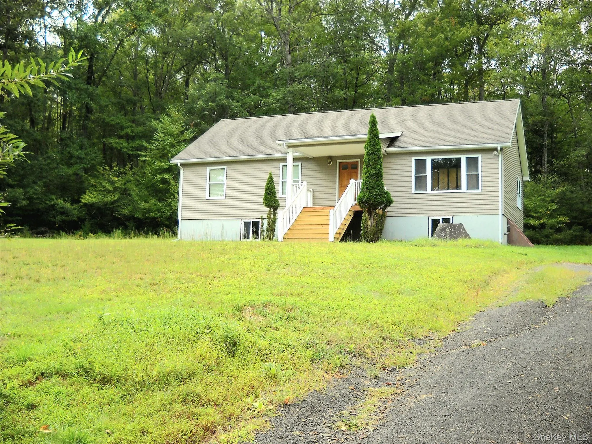 View of front of home featuring a front lawn, a shingled roof, view of wooded area, and a porch View of front of home featuring a front lawn, a shingled roof, view of wooded area, and a porch