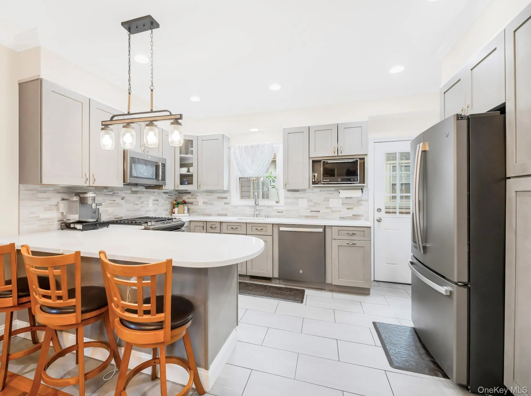 Kitchen with a peninsula, light countertops, a kitchen breakfast bar, appliances with stainless steel finishes, and decorative light fixtures Kitchen with a peninsula, light countertops, a kitchen breakfast bar, appliances with stainless steel finishes, and decorative light fixtures