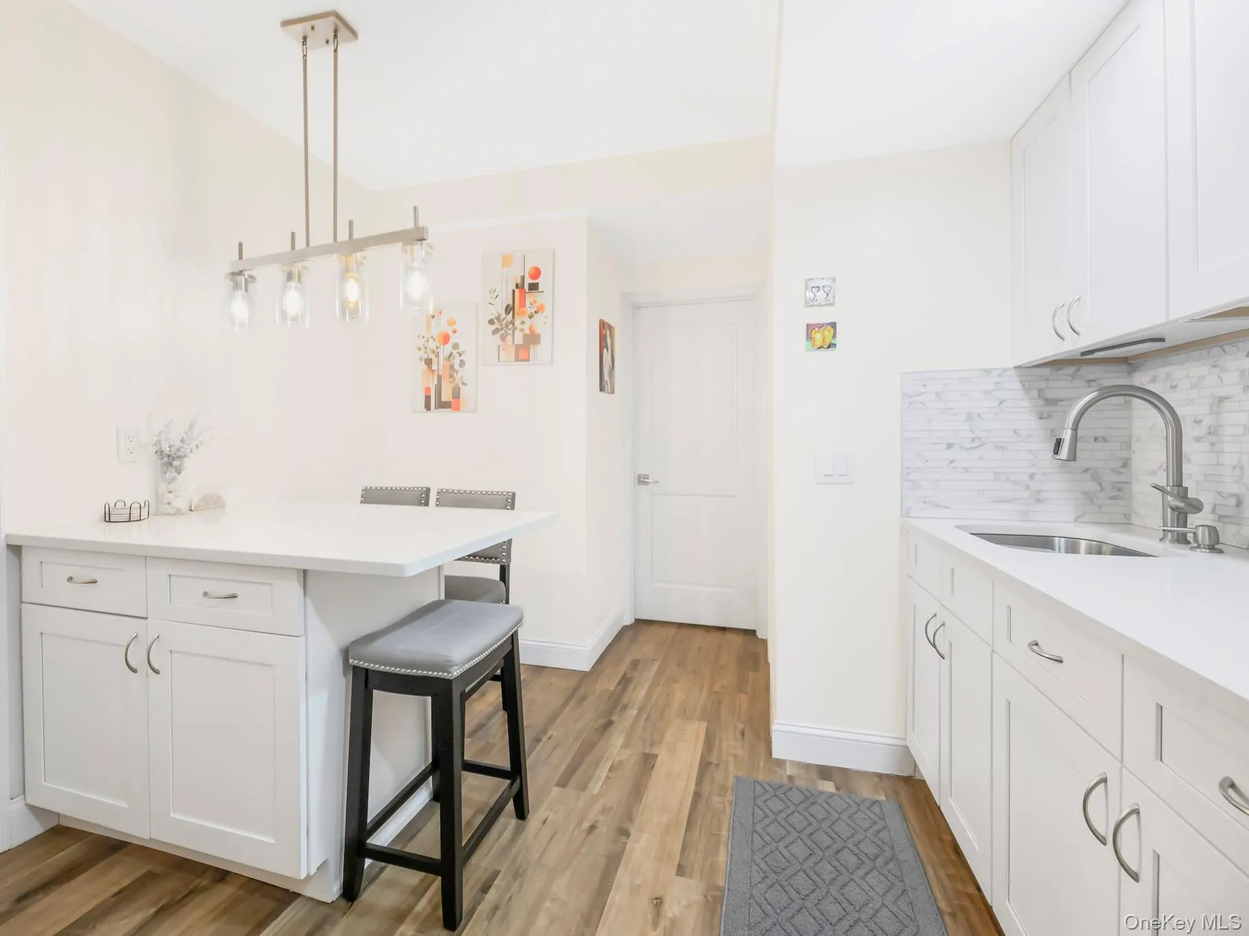 Kitchen with white cabinets, decorative light fixtures, a breakfast bar area, a peninsula, and tasteful backsplash Kitchen with white cabinets, decorative light fixtures, a breakfast bar area, a peninsula, and tasteful backsplash