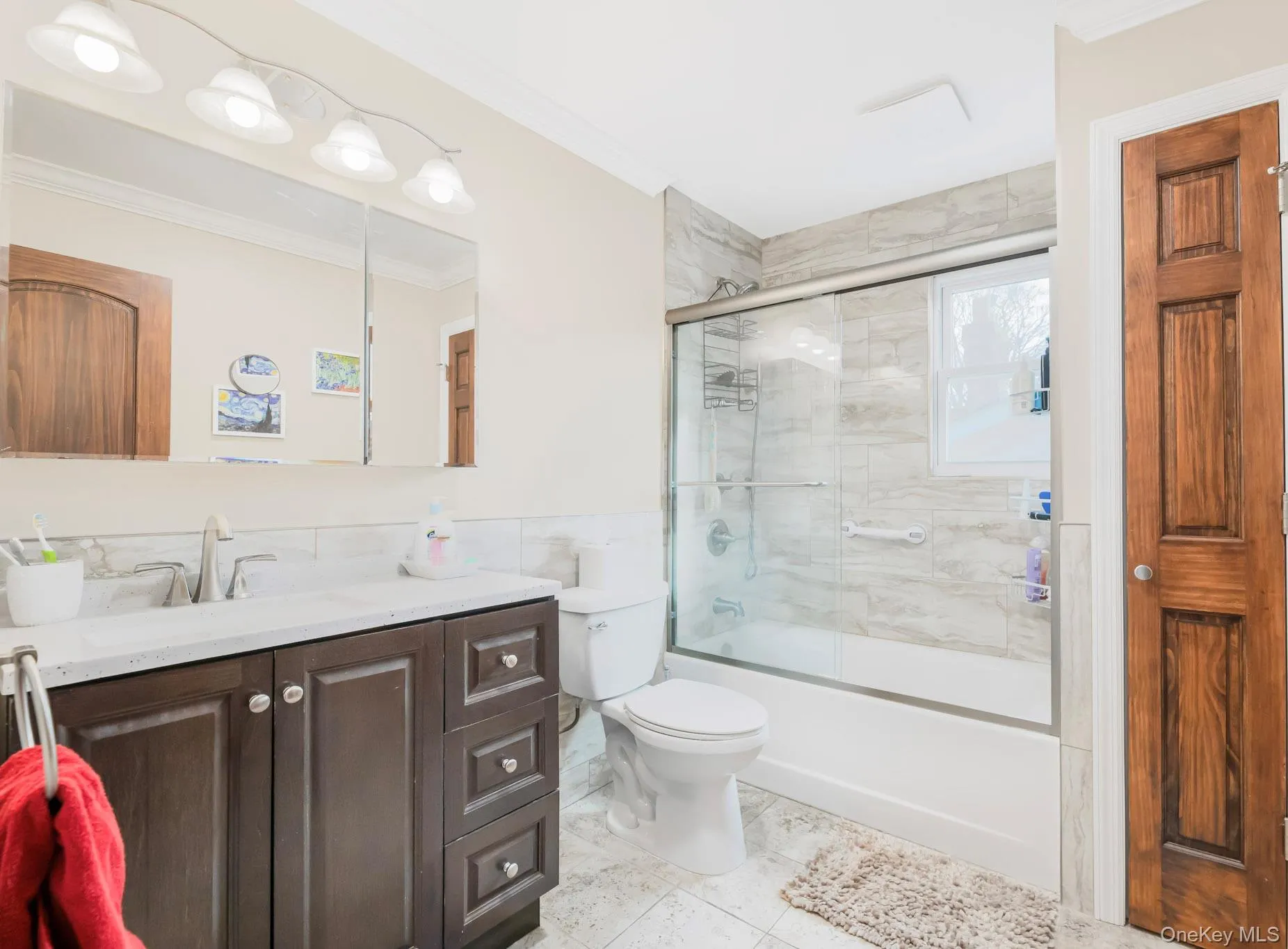 Full bathroom with vanity, bath / shower combo with glass door, crown molding, tile walls, and wainscoting Full bathroom with vanity, bath / shower combo with glass door, crown molding, tile walls, and wainscoting
