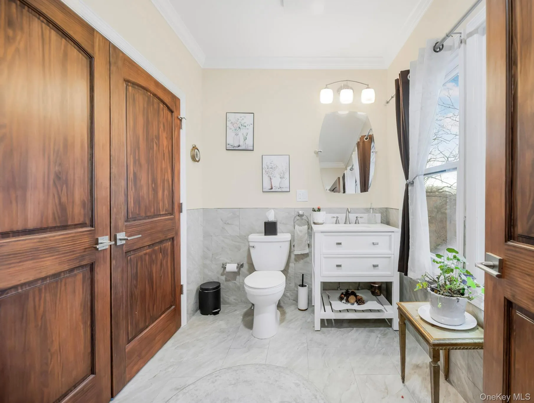 Bathroom with tile walls, wainscoting, crown molding, vanity, and light marble finish floors Bathroom with tile walls, wainscoting, crown molding, vanity, and light marble finish floors