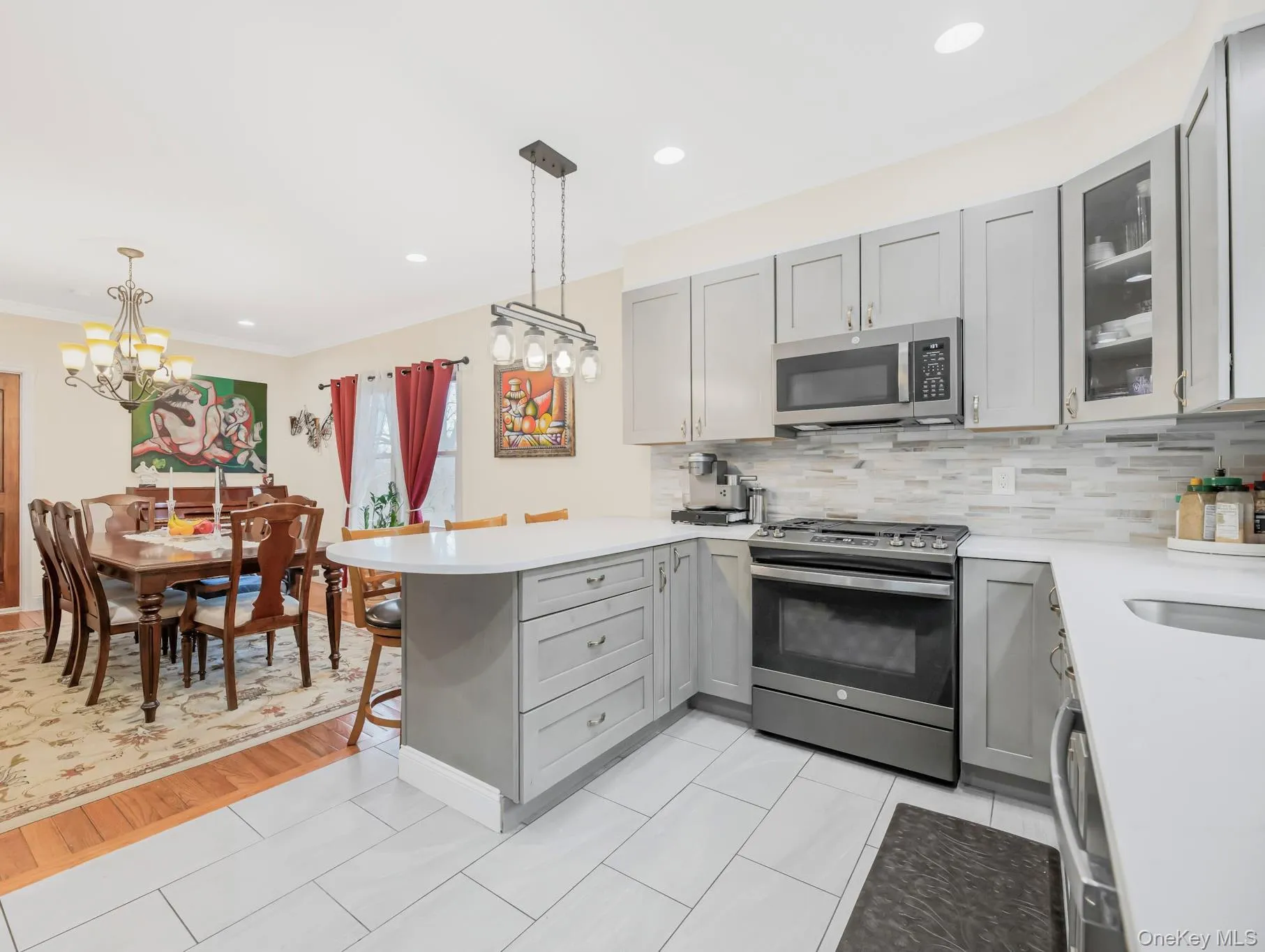 Kitchen featuring gray cabinetry, a peninsula, stainless steel appliances, pendant lighting, and glass insert cabinets Kitchen featuring gray cabinetry, a peninsula, stainless steel appliances, pendant lighting, and glass insert cabinets
