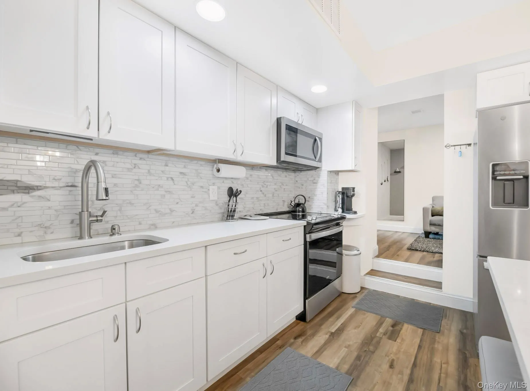 Kitchen with white cabinetry, appliances with stainless steel finishes, tasteful backsplash, light wood-style floors, and light stone countertops Kitchen with white cabinetry, appliances with stainless steel finishes, tasteful backsplash, light wood-style floors, and light stone countertops