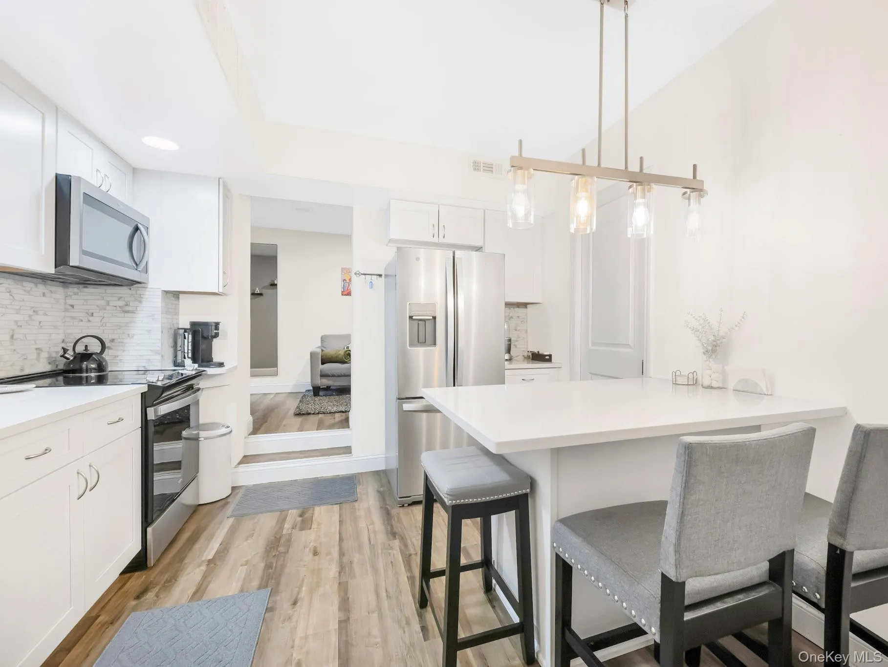 Kitchen featuring appliances with stainless steel finishes, a breakfast bar, tasteful backsplash, white cabinets, and a peninsula Kitchen featuring appliances with stainless steel finishes, a breakfast bar, tasteful backsplash, white cabinets, and a peninsula