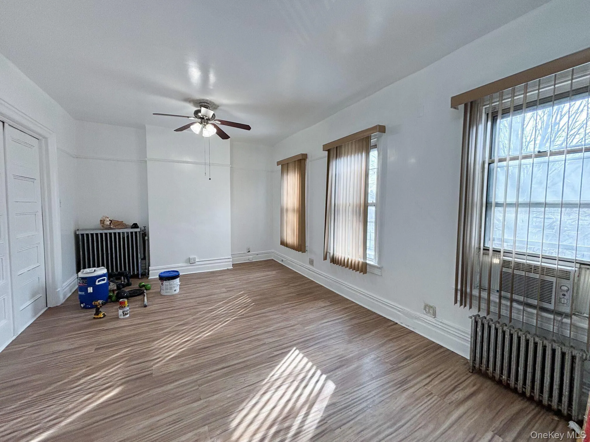 Unfurnished living room with radiator, a ceiling fan, cooling unit, and wood finished floors Unfurnished living room with radiator, a ceiling fan, cooling unit, and wood finished floors