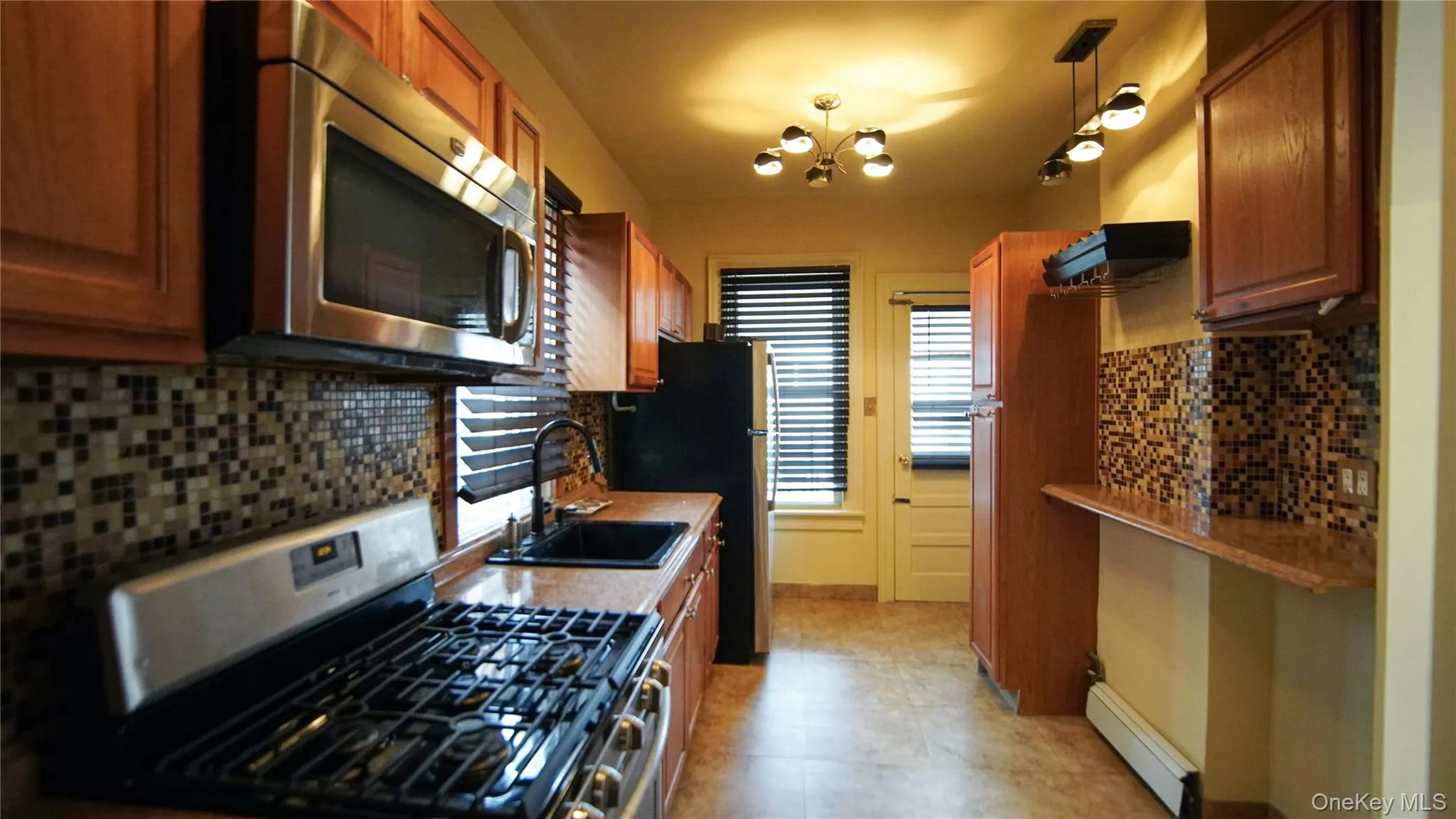 Kitchen featuring stainless steel appliances, wood finish cabinetry, baseboard heating, and tasteful backsplash Kitchen featuring stainless steel appliances, wood finish cabinetry, baseboard heating, and tasteful backsplash