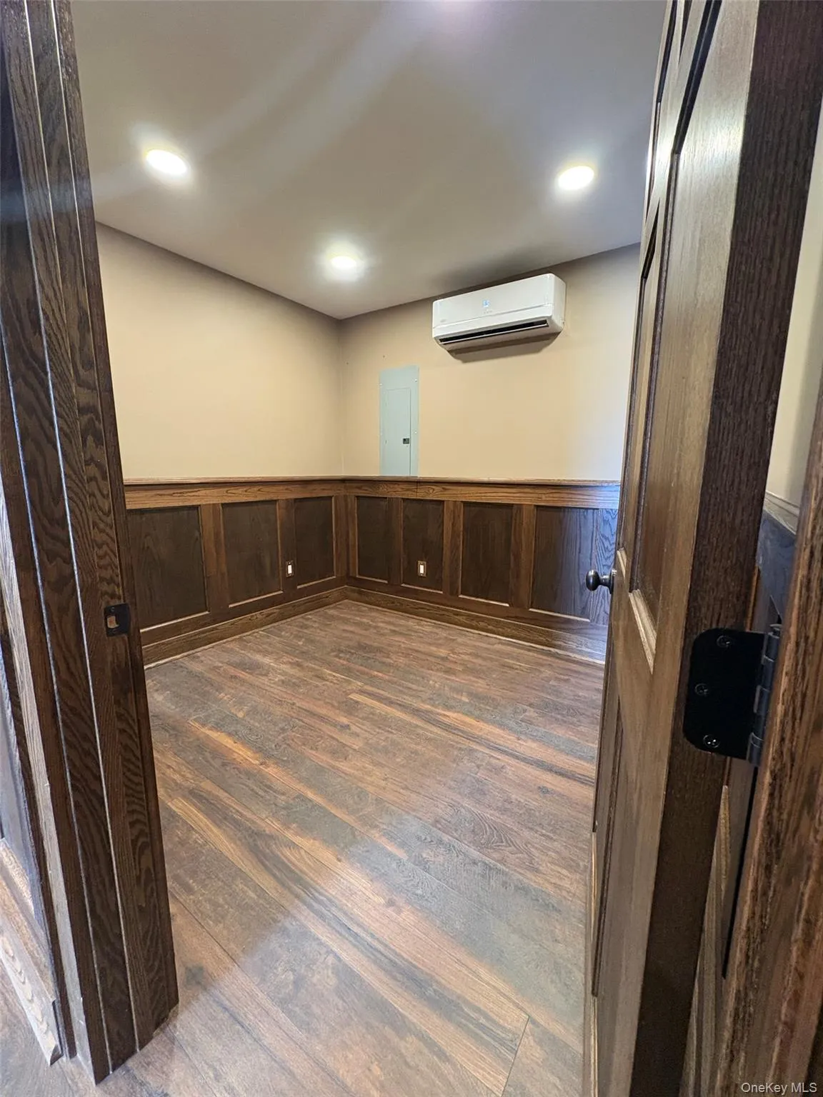 Unfurnished room featuring wainscoting, dark wood-style flooring, wood walls, recessed lighting, and electric panel Unfurnished room featuring wainscoting, dark wood-style flooring, wood walls, recessed lighting, and electric panel