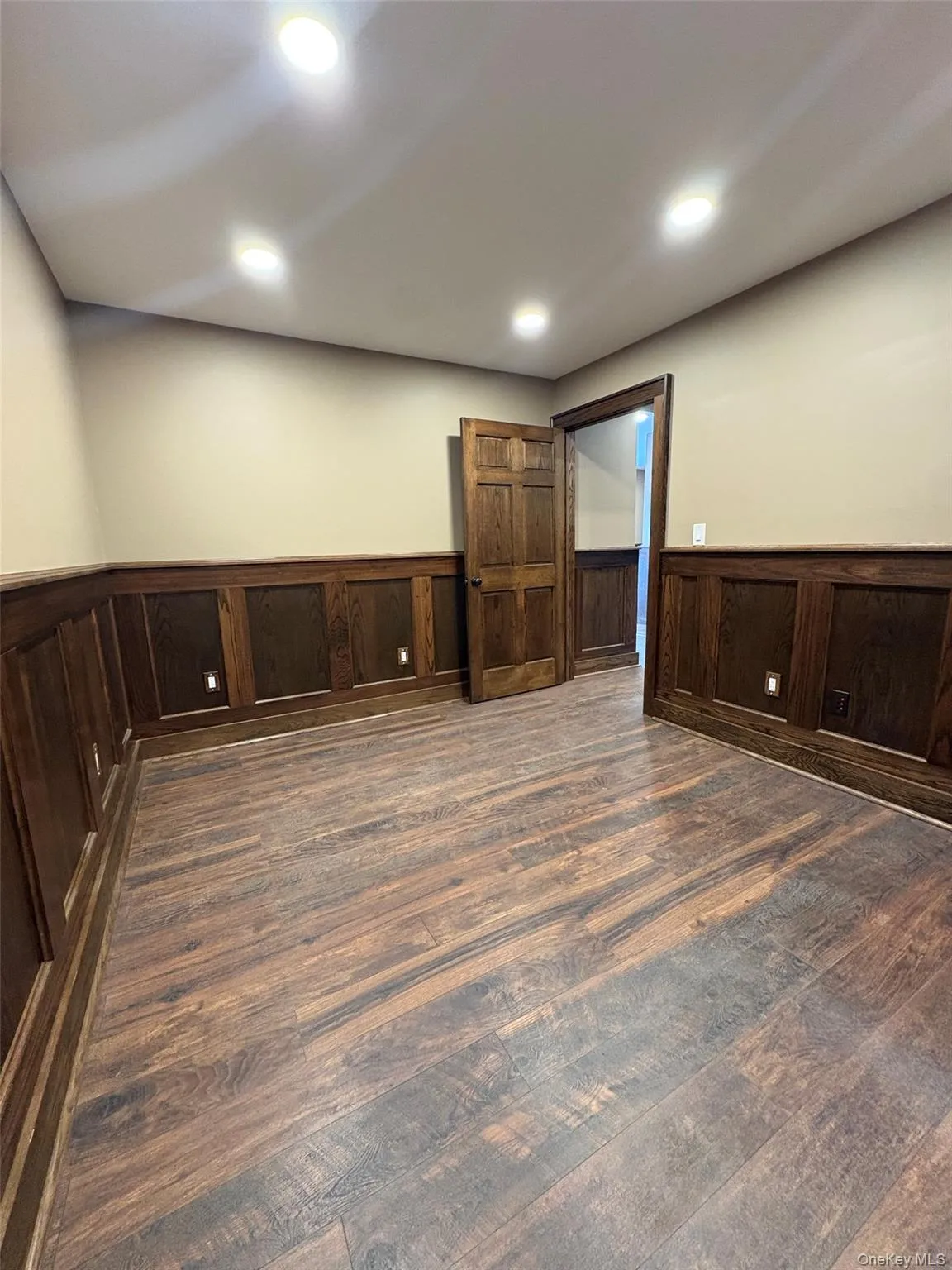 Empty room with a wainscoted wall, recessed lighting, and dark wood-type flooring Empty room with a wainscoted wall, recessed lighting, and dark wood-type flooring