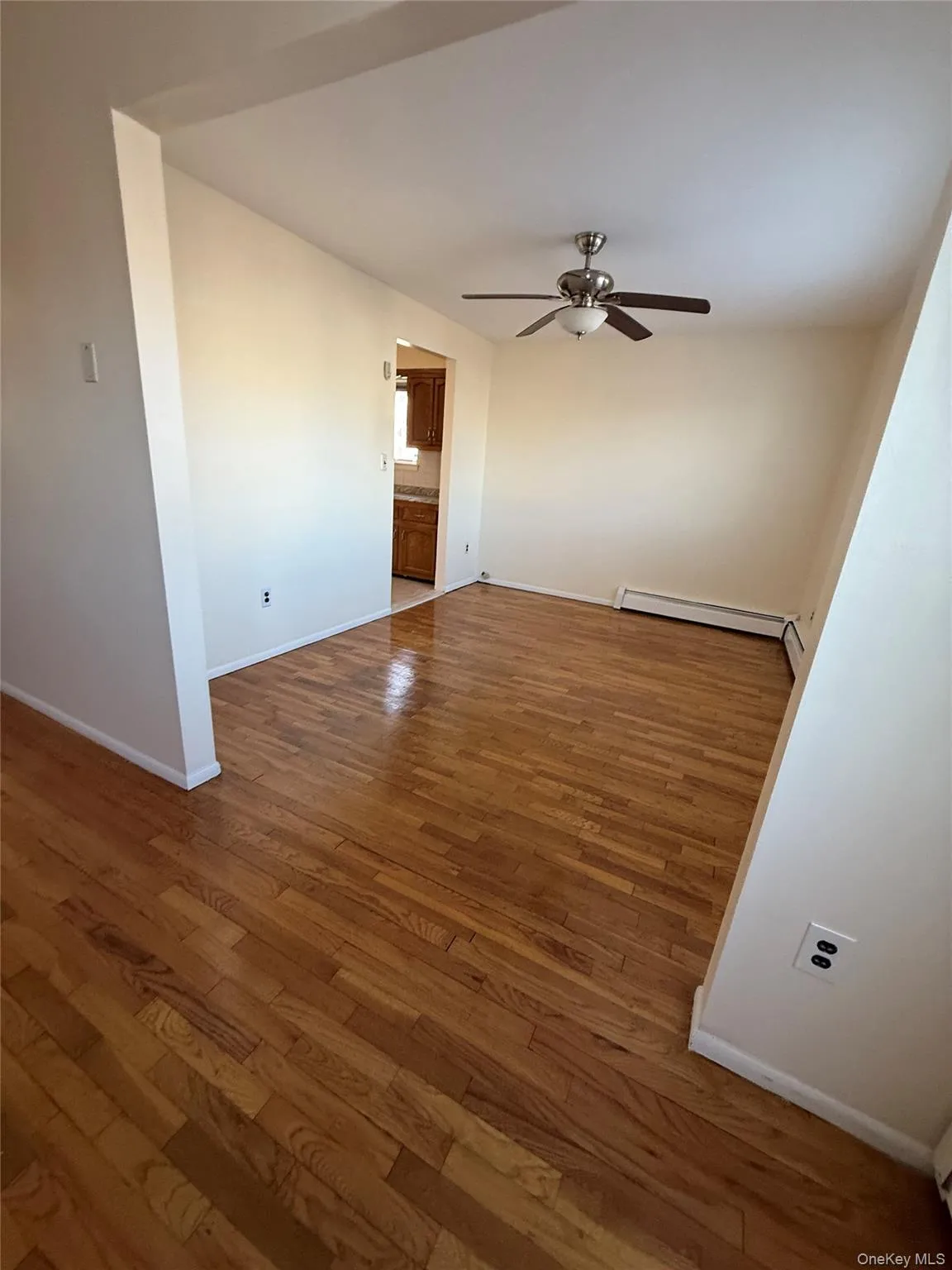 Unfurnished room featuring light wood-style flooring, a ceiling fan, and a baseboard radiator Unfurnished room featuring light wood-style flooring, a ceiling fan, and a baseboard radiator