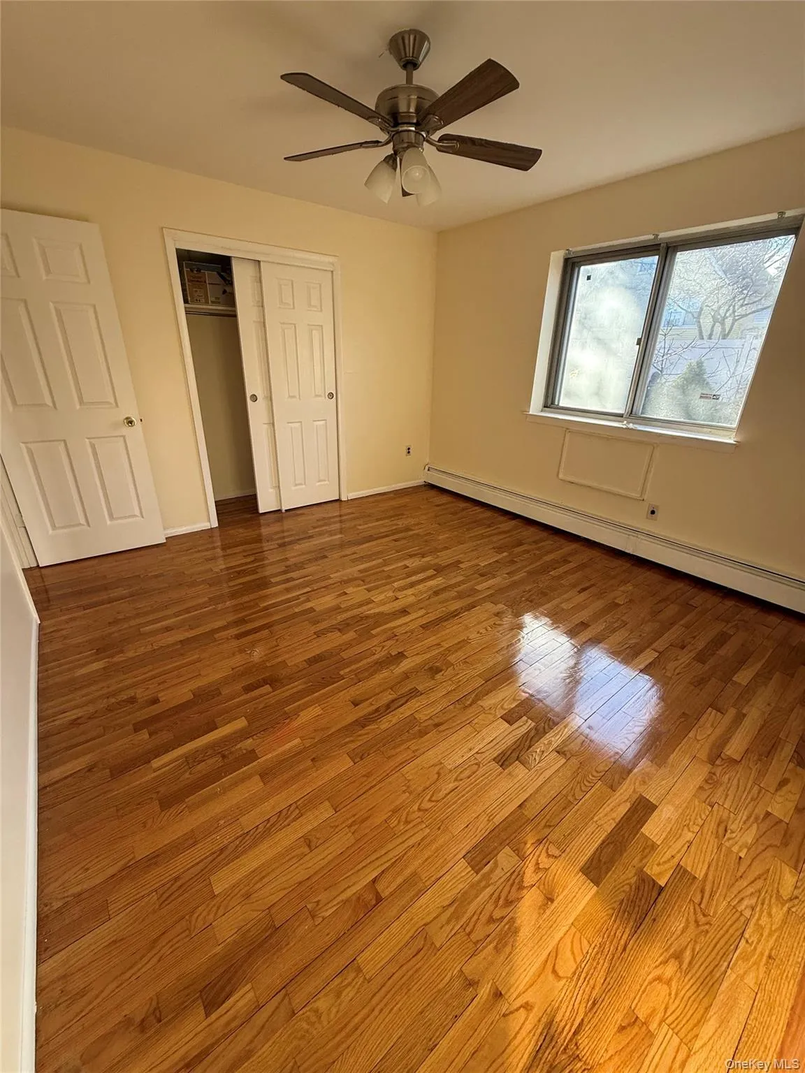 Unfurnished bedroom with a baseboard heating unit, wood finished floors, a closet, and a ceiling fan Unfurnished bedroom with a baseboard heating unit, wood finished floors, a closet, and a ceiling fan