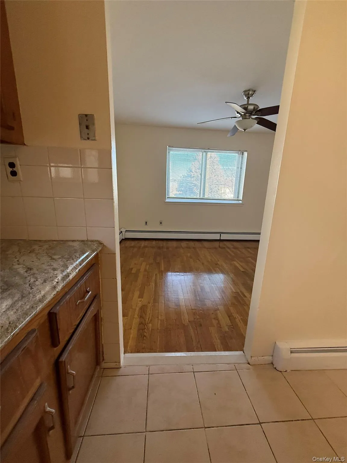 Kitchen with brown cabinetry, light stone counters, baseboard heating, and light tile patterned floors Kitchen with brown cabinetry, light stone counters, baseboard heating, and light tile patterned floors