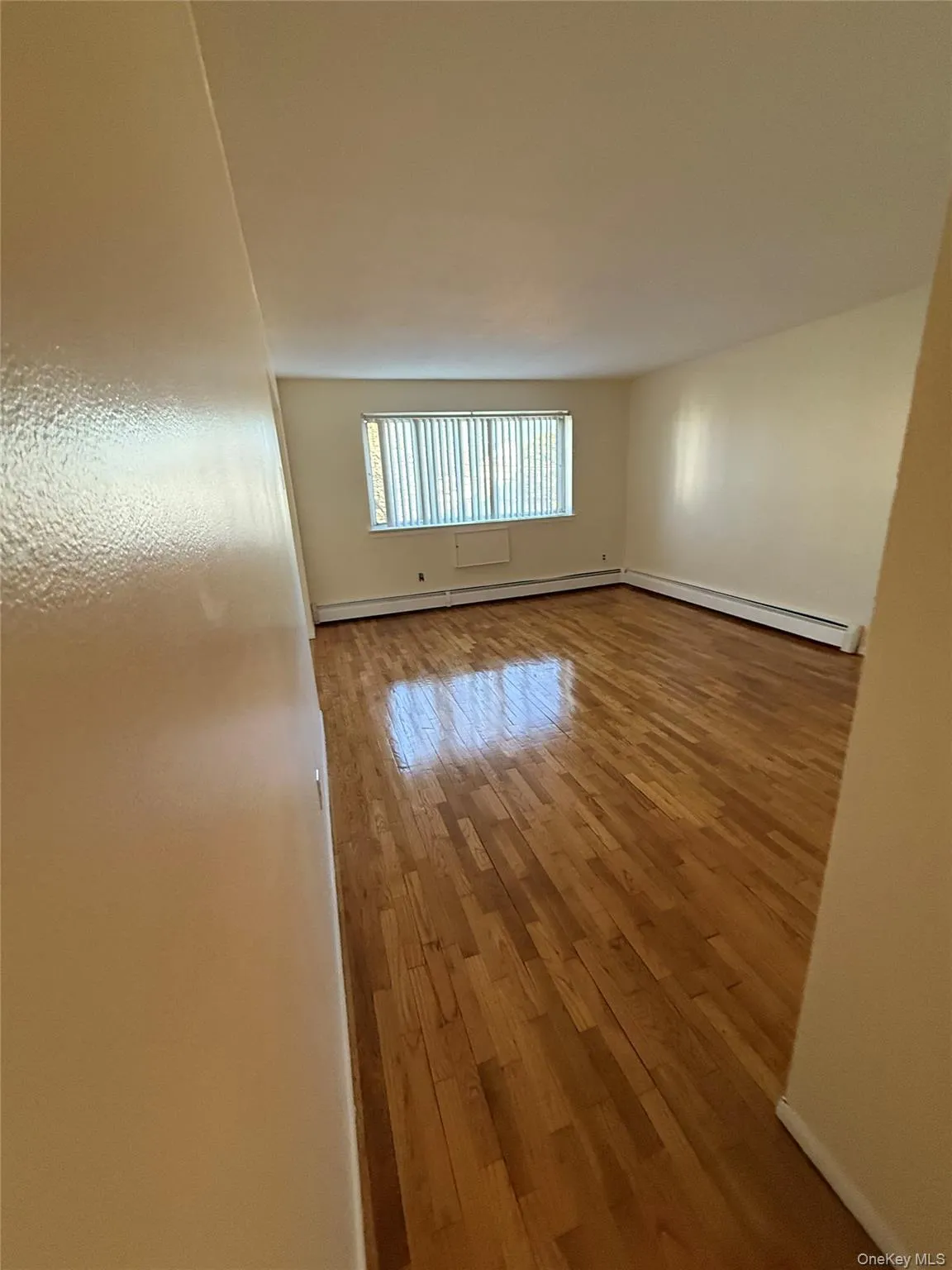 Unfurnished room with wood finished floors and baseboard heating Unfurnished room with wood finished floors and baseboard heating