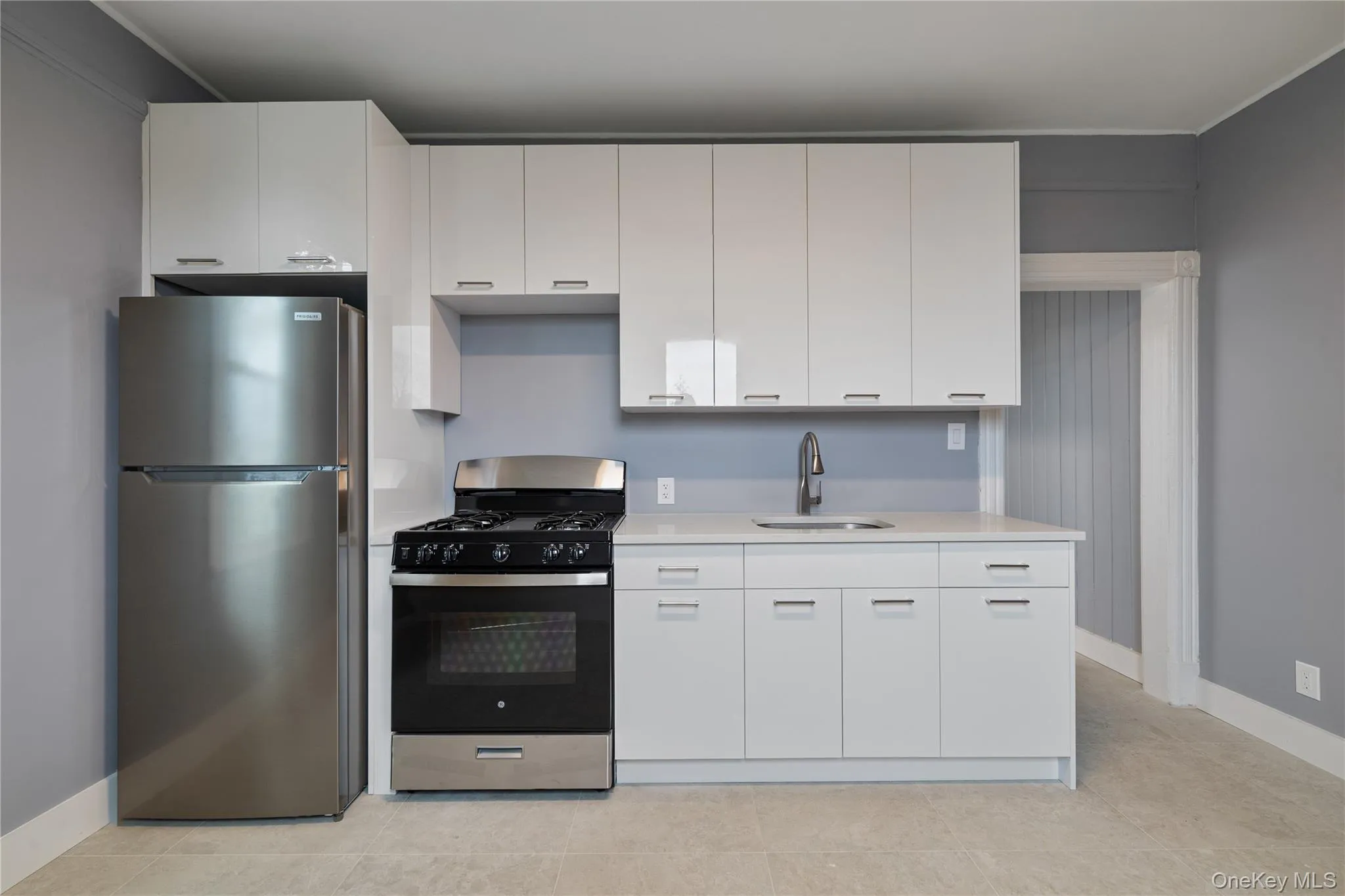 Kitchen with range with gas stovetop, light countertops, freestanding refrigerator, white cabinets, and a sink Kitchen with range with gas stovetop, light countertops, freestanding refrigerator, white cabinets, and a sink