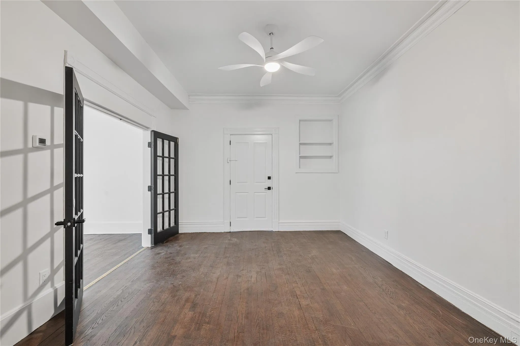 Empty room with dark wood-type flooring, baseboards, crown molding, and ceiling fan Empty room with dark wood-type flooring, baseboards, crown molding, and ceiling fan