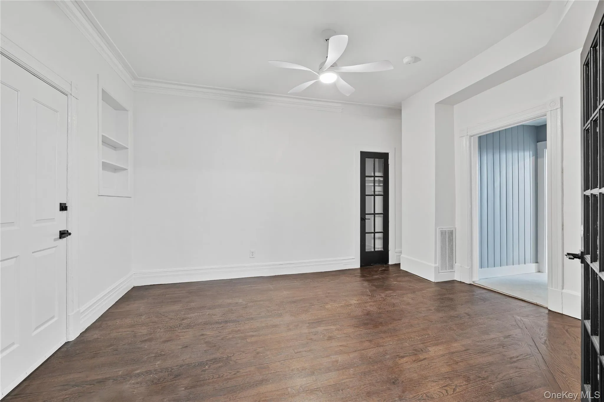 Unfurnished room with dark wood-style flooring, ornamental molding, a ceiling fan, visible vents, and built in shelves Unfurnished room with dark wood-style flooring, ornamental molding, a ceiling fan, visible vents, and built in shelves