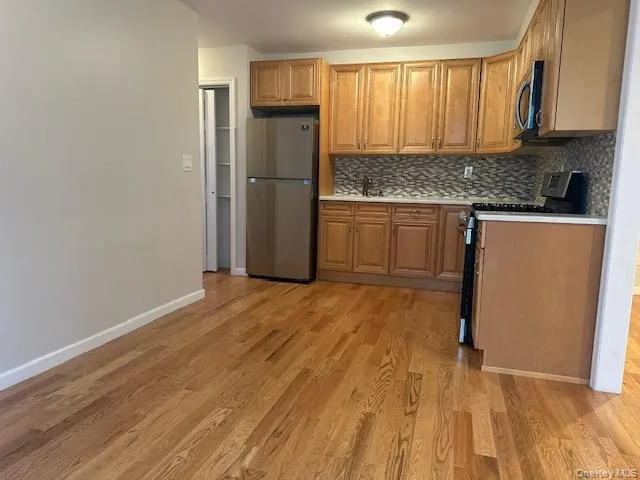 Kitchen featuring stainless steel appliances, brown cabinetry, light wood-style flooring, and decorative backsplash Kitchen featuring stainless steel appliances, brown cabinetry, light wood-style flooring, and decorative backsplash