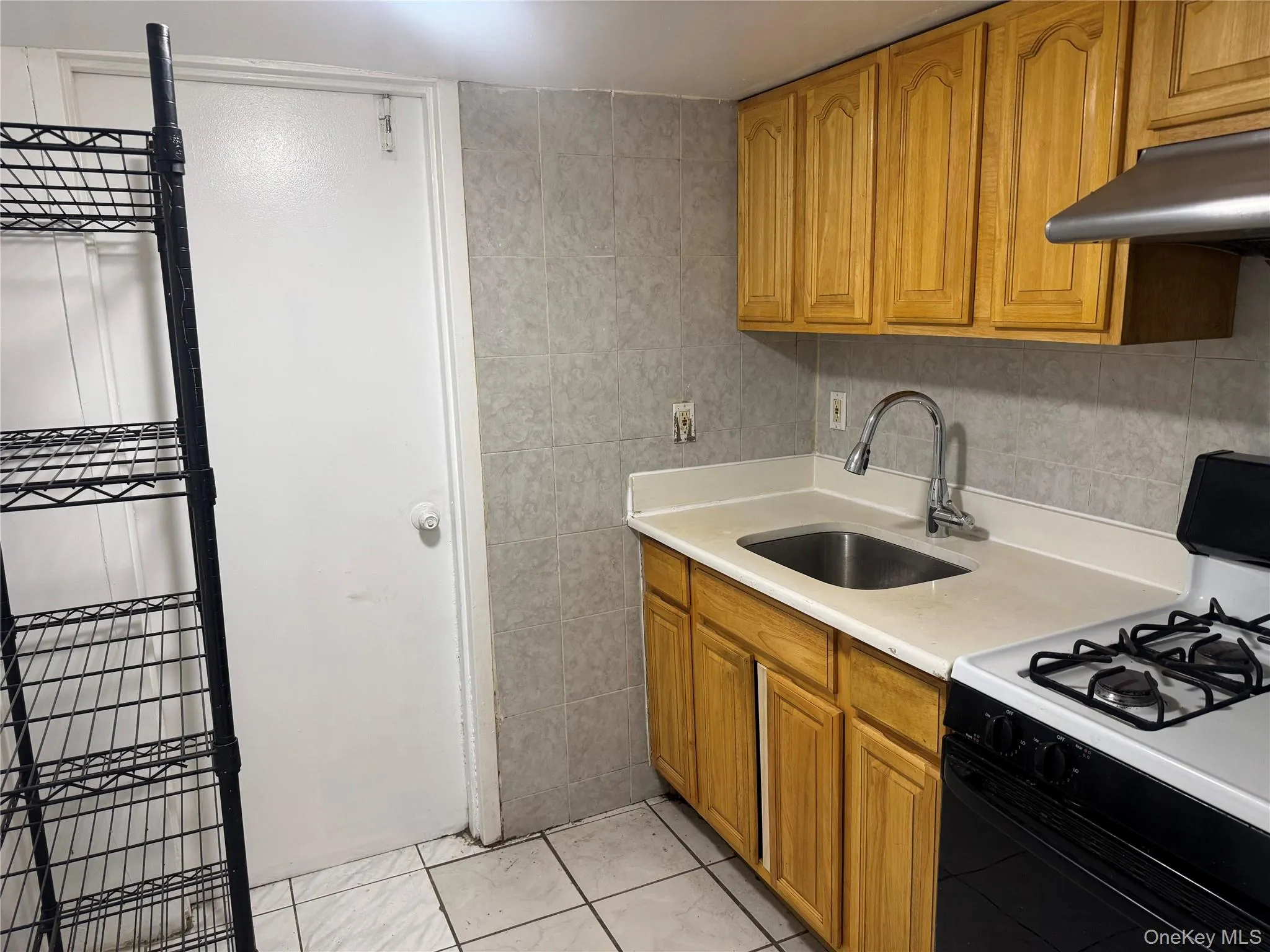 Kitchen featuring range with gas stovetop, brown cabinets, light countertops, tile walls, and under cabinet range hood Kitchen featuring range with gas stovetop, brown cabinets, light countertops, tile walls, and under cabinet range hood