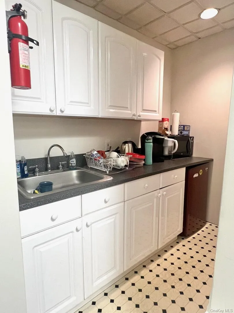 Kitchen featuring dark countertops, white cabinets, a drop ceiling, and light flooring Kitchen featuring dark countertops, white cabinets, a drop ceiling, and light flooring