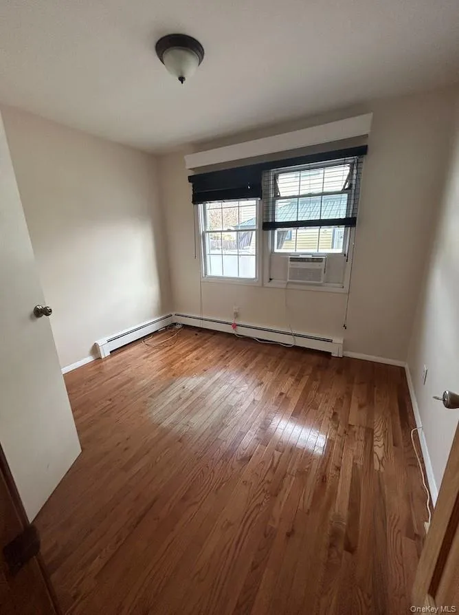 Spare room with light wood-style floors, a baseboard heating unit, and cooling unit Spare room with light wood-style floors, a baseboard heating unit, and cooling unit