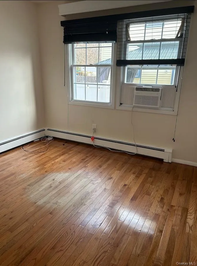 Empty room featuring light wood-type flooring, a baseboard radiator, and cooling unit Empty room featuring light wood-type flooring, a baseboard radiator, and cooling unit
