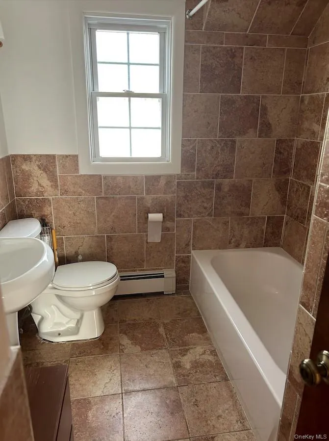 Full bath featuring tile walls, shower / washtub combination, a baseboard heating unit, and wainscoting Full bath featuring tile walls, shower / washtub combination, a baseboard heating unit, and wainscoting