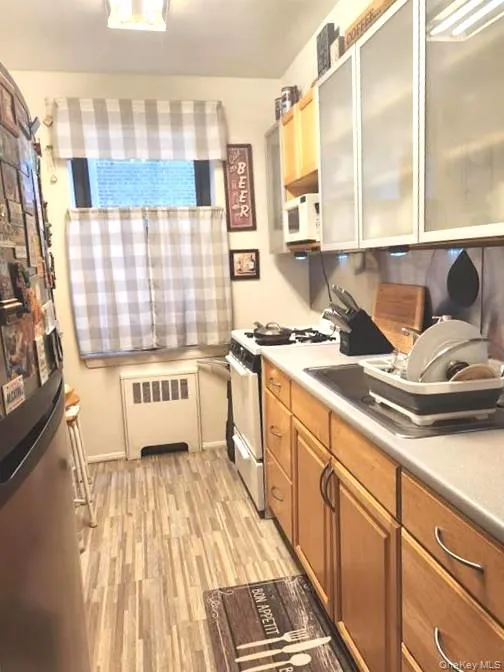 Kitchen with freestanding refrigerator, light wood-type flooring, radiator, light countertops, and range with electric cooktop Kitchen with freestanding refrigerator, light wood-type flooring, radiator, light countertops, and range with electric cooktop