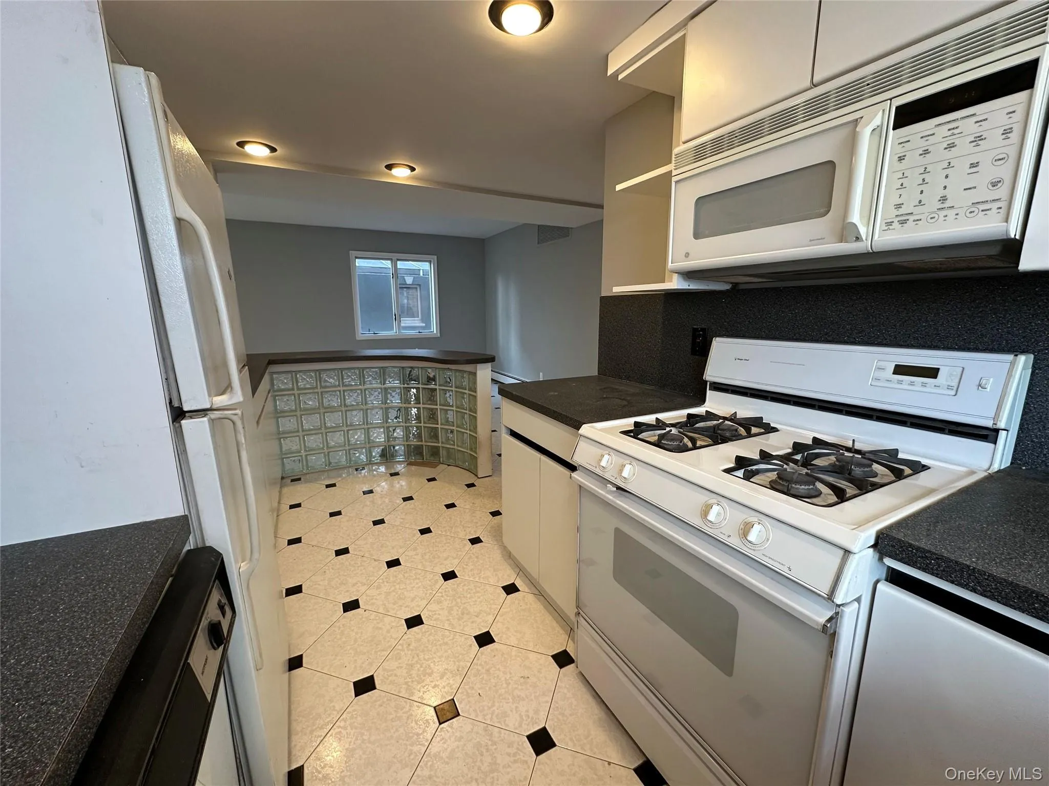 Kitchen featuring white appliances, dark countertops, white cabinets, and light tile patterned floors Kitchen featuring white appliances, dark countertops, white cabinets, and light tile patterned floors