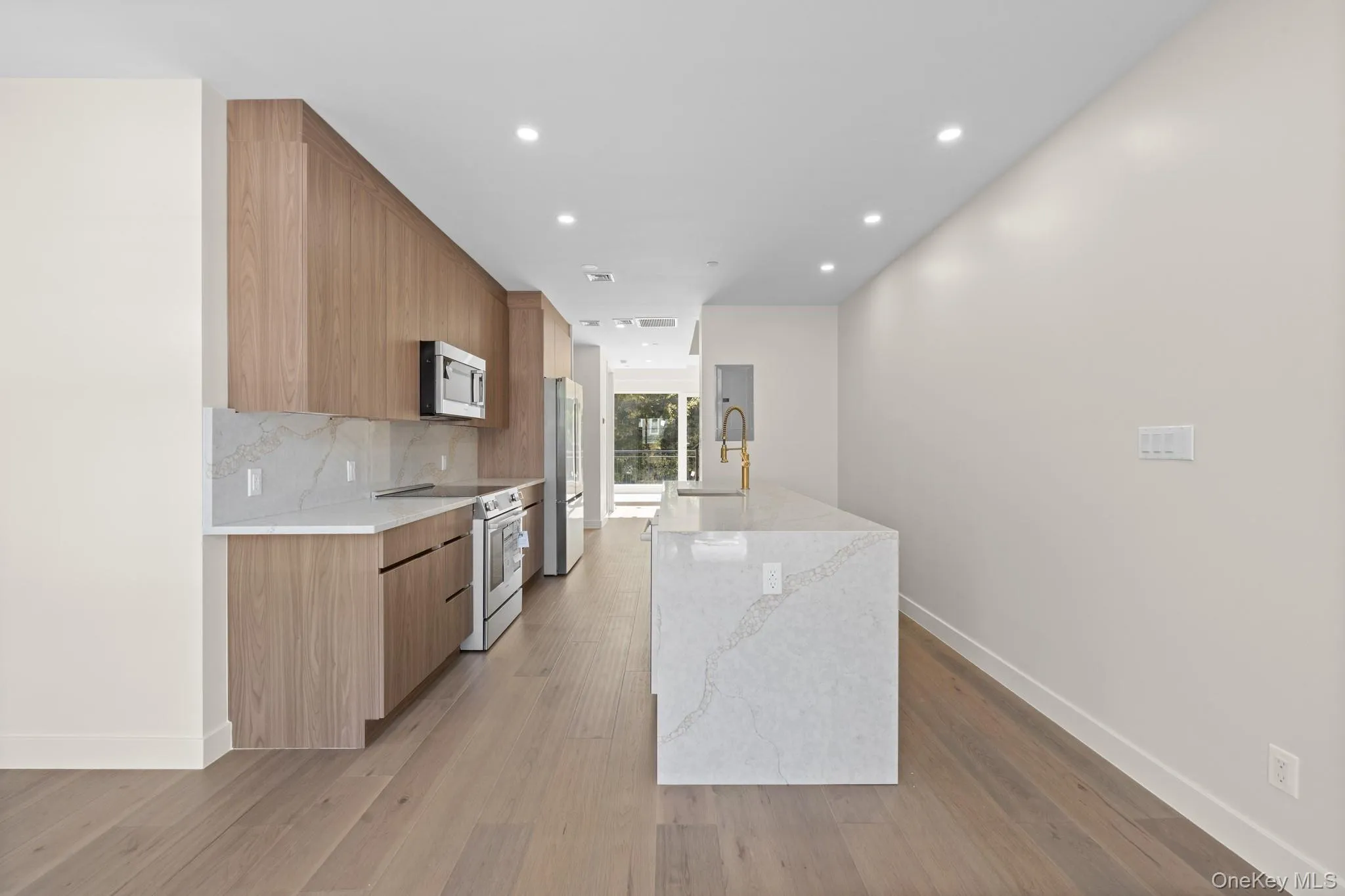Kitchen with modern cabinets, light stone countertops, appliances with stainless steel finishes, light wood finished floors, and recessed lighting Kitchen with modern cabinets, light stone countertops, appliances with stainless steel finishes, light wood finished floors, and recessed lighting