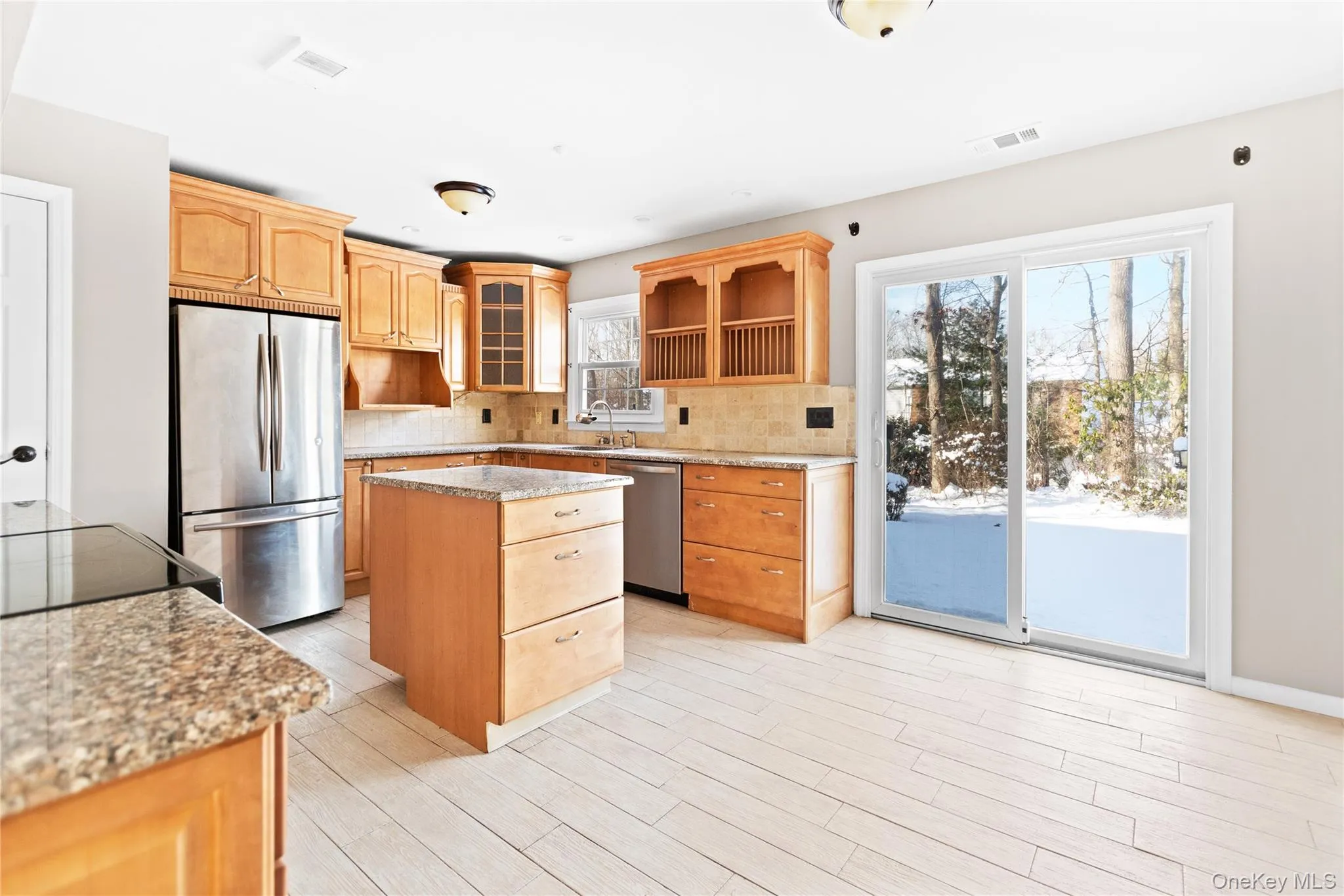 Kitchen featuring stainless steel appliances, light Granite countertops, a kitchen island, backsplash, and tile wood-style floors Kitchen featuring stainless steel appliances, light Granite countertops, a kitchen island, backsplash, and tile wood-style floors