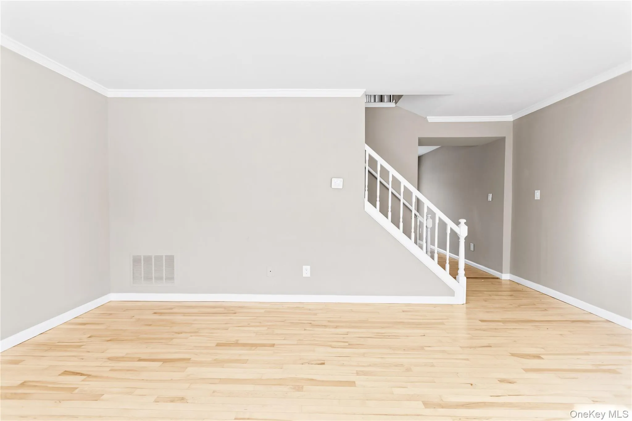 Empty room with stairs, crown molding, and light wood finished floors Empty room with stairs, crown molding, and light wood finished floors