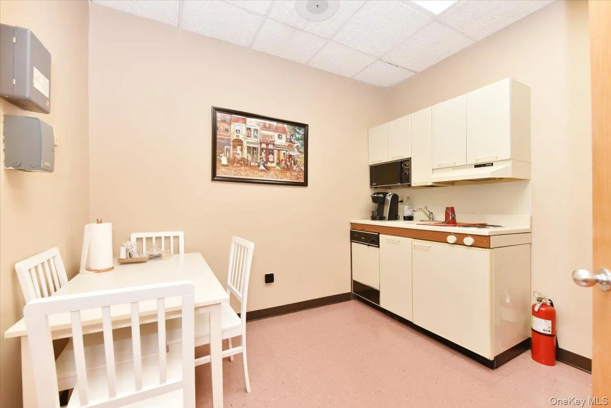 Kitchen featuring light countertops, a drop ceiling, black microwave, white cabinetry, and dishwasher Kitchen featuring light countertops, a drop ceiling, black microwave, white cabinetry, and dishwasher